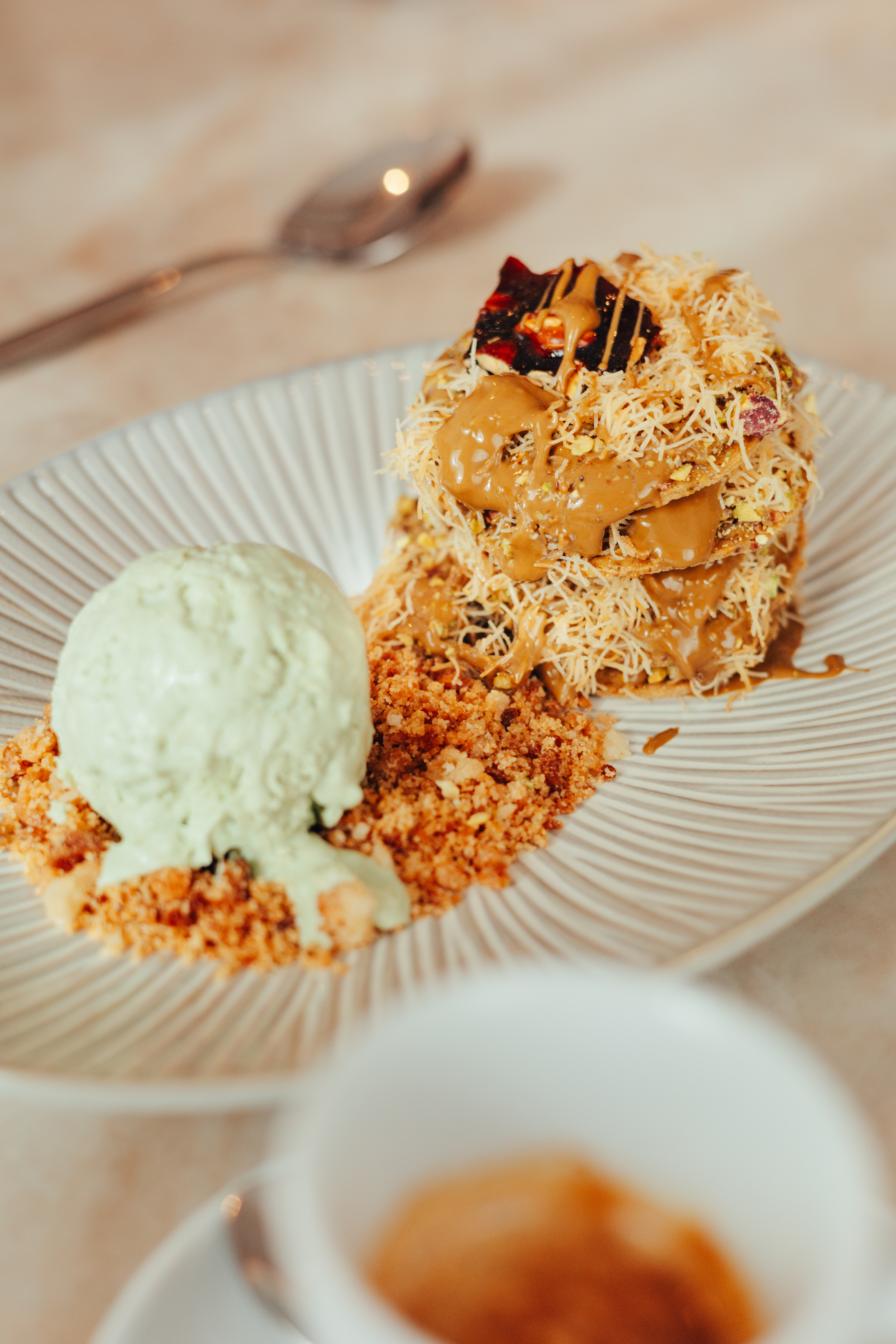 Stacked kunafa dessert with caramel, pistachios, and green ice cream.