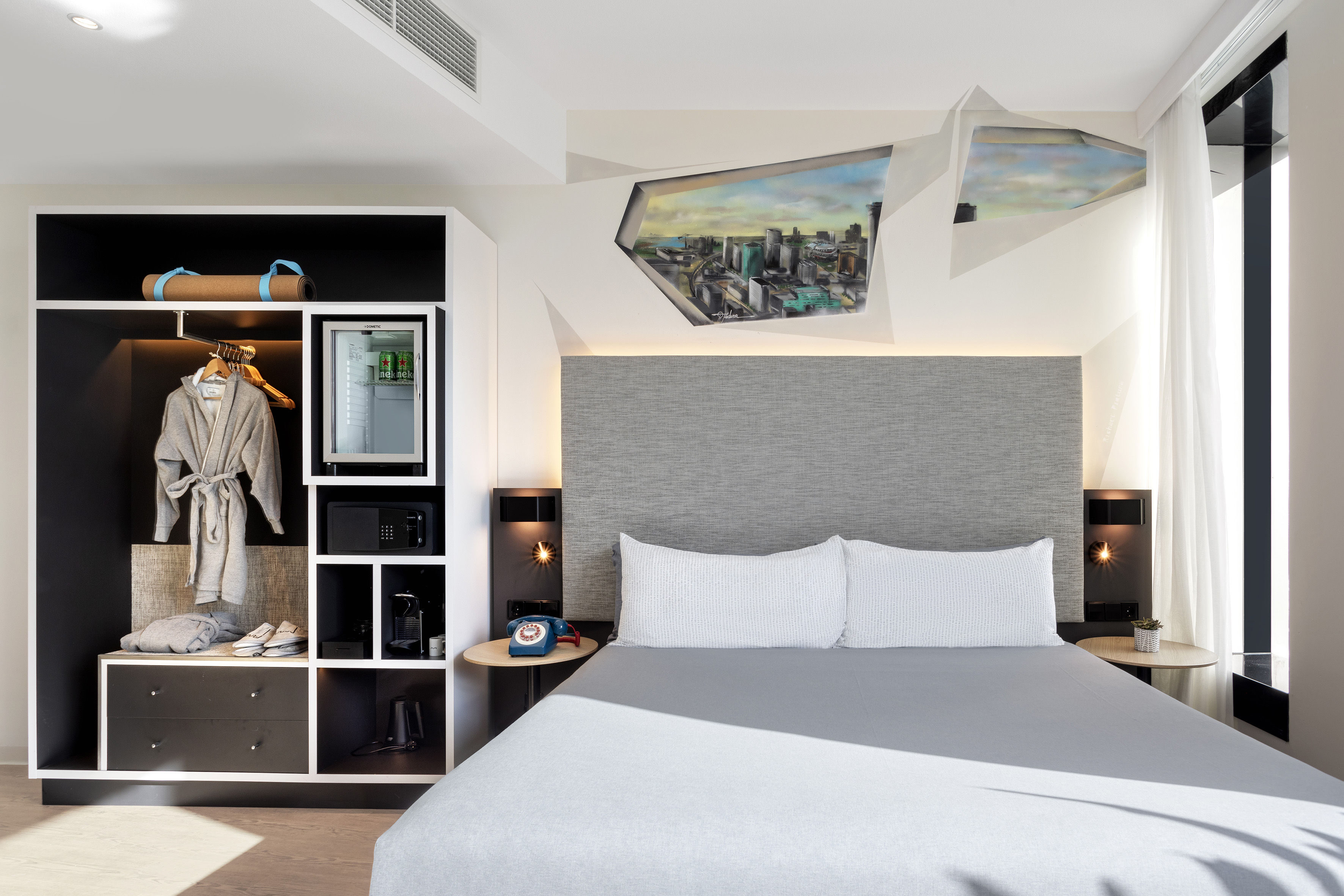 Modern hotel room with grey bed, city art, integrated wardrobe, mini-bar.