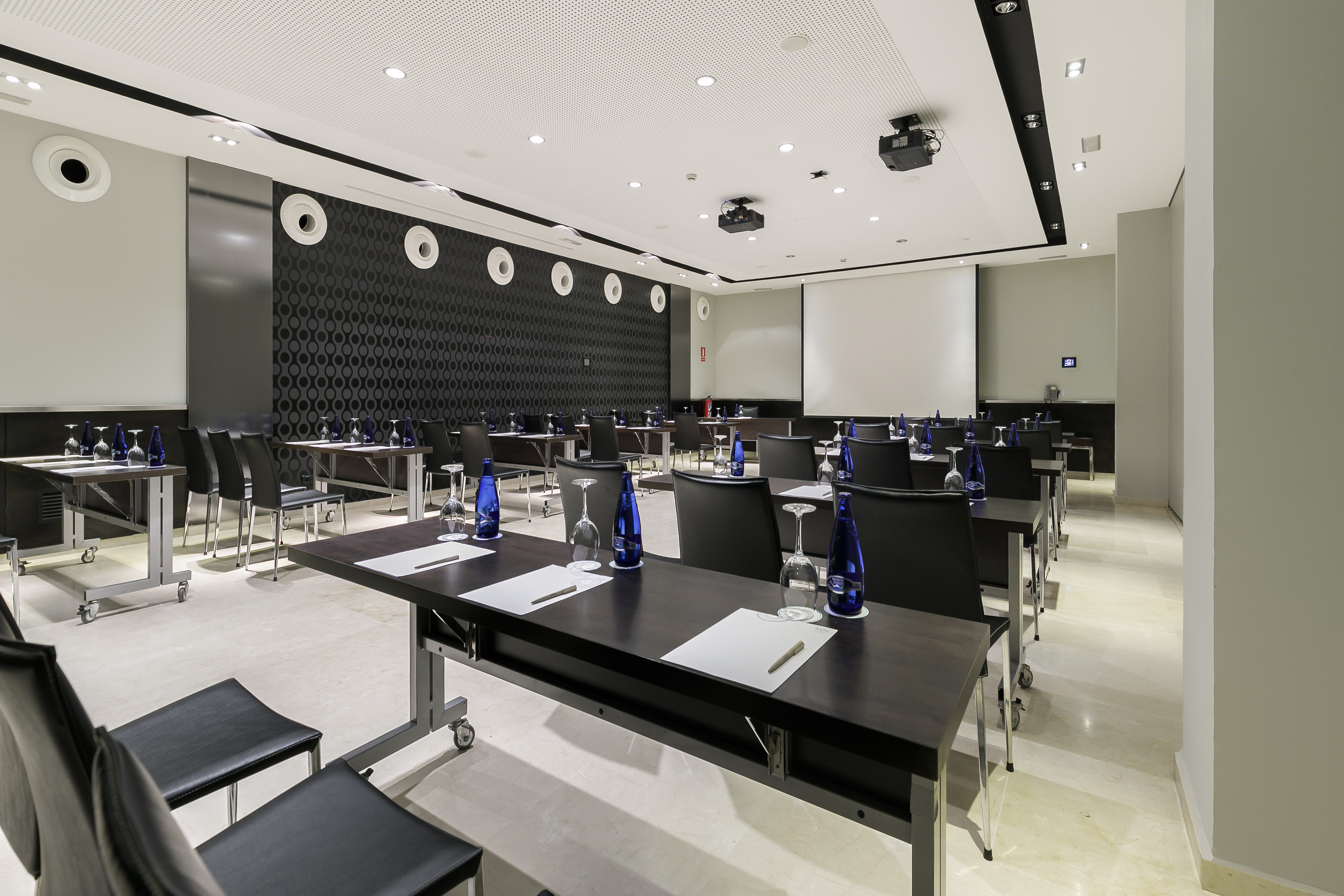 Modern conference room with tables, chairs, projector, and large screen.