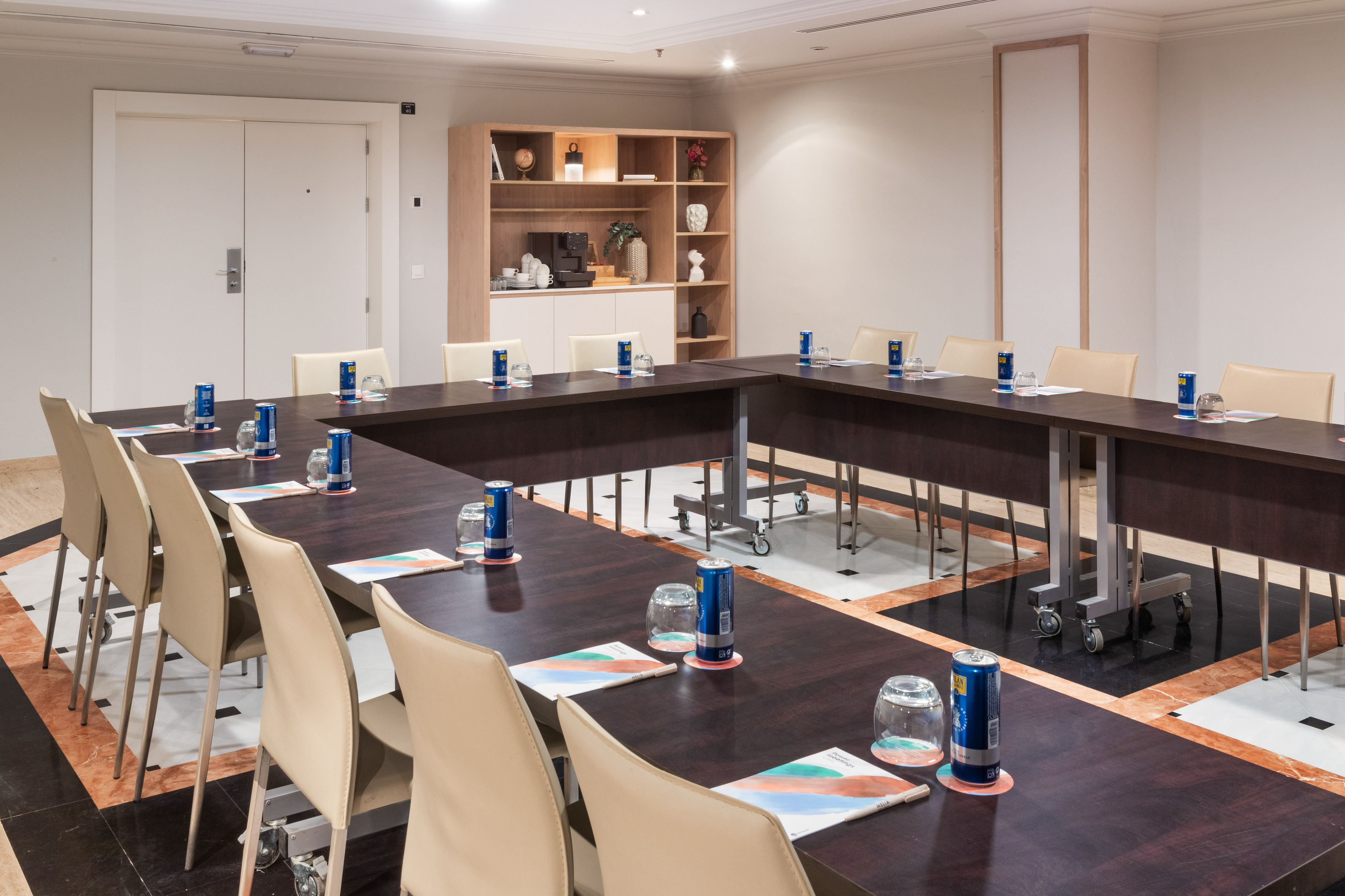 Hotel conference room with U-shaped table, beige chairs, and coffee station.
