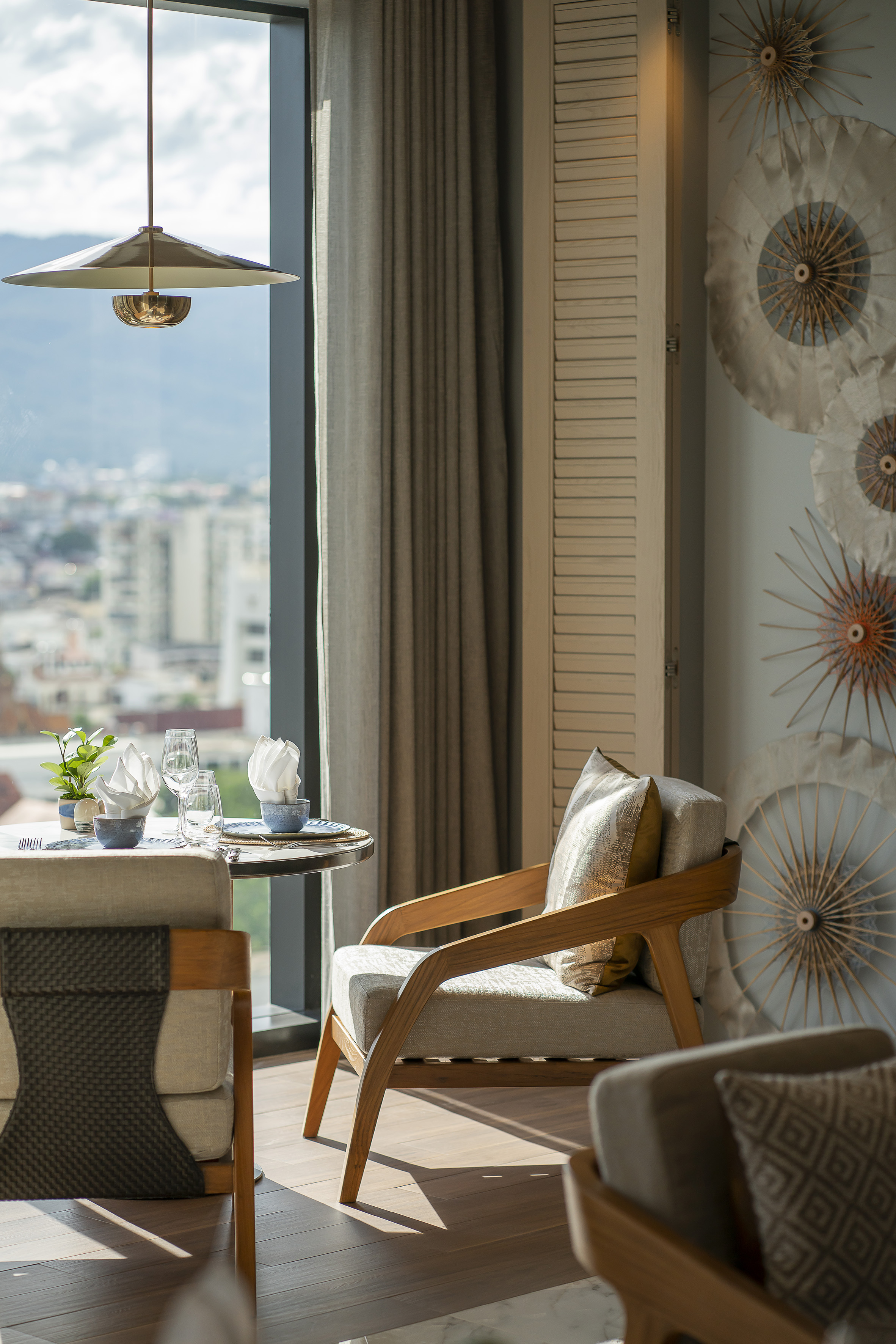 Modern hotel room dining area with city view, stylish chairs, and unique wall decor.