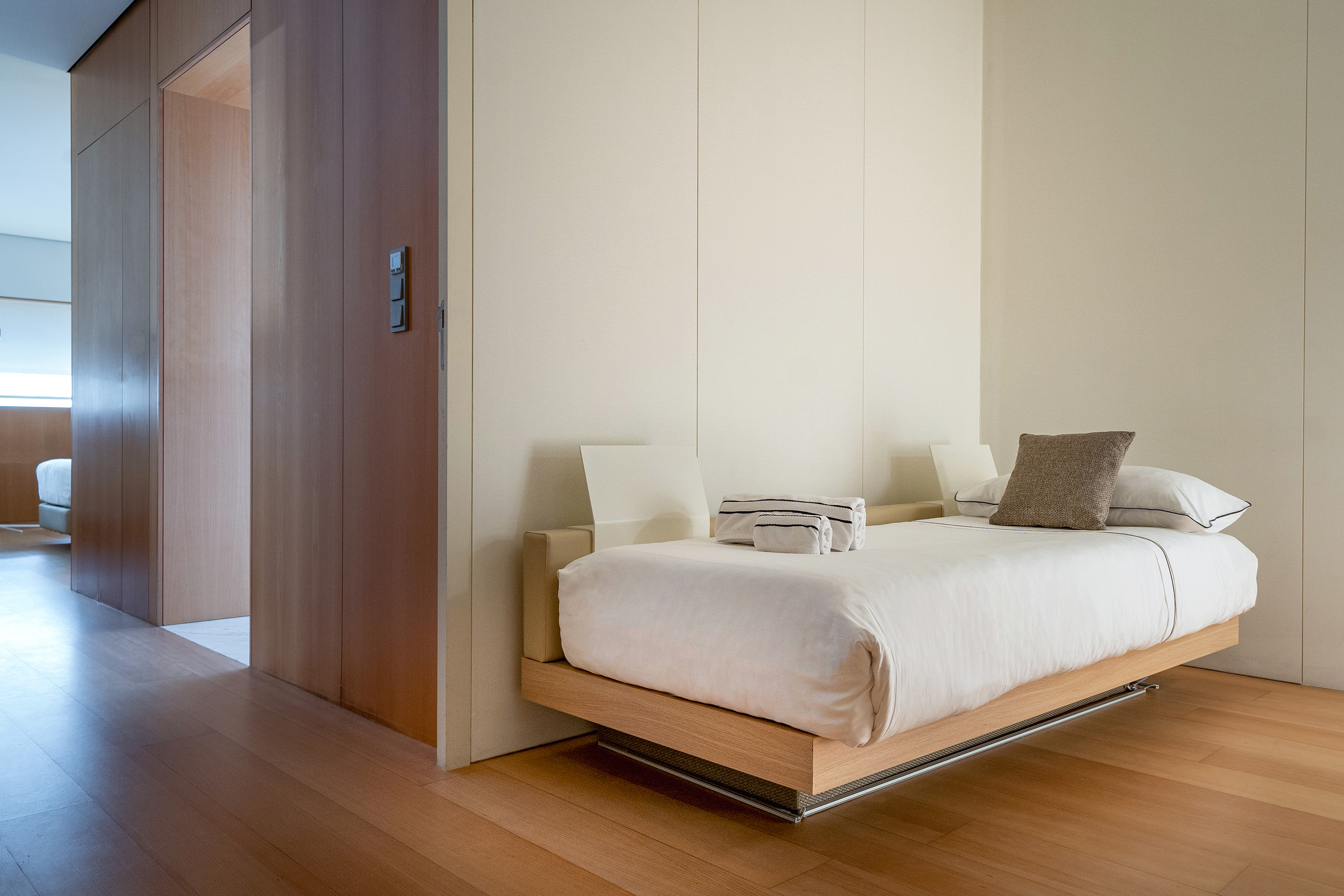 Sleek modern bedroom with floating wood bed, white linen, and hardwood floor.