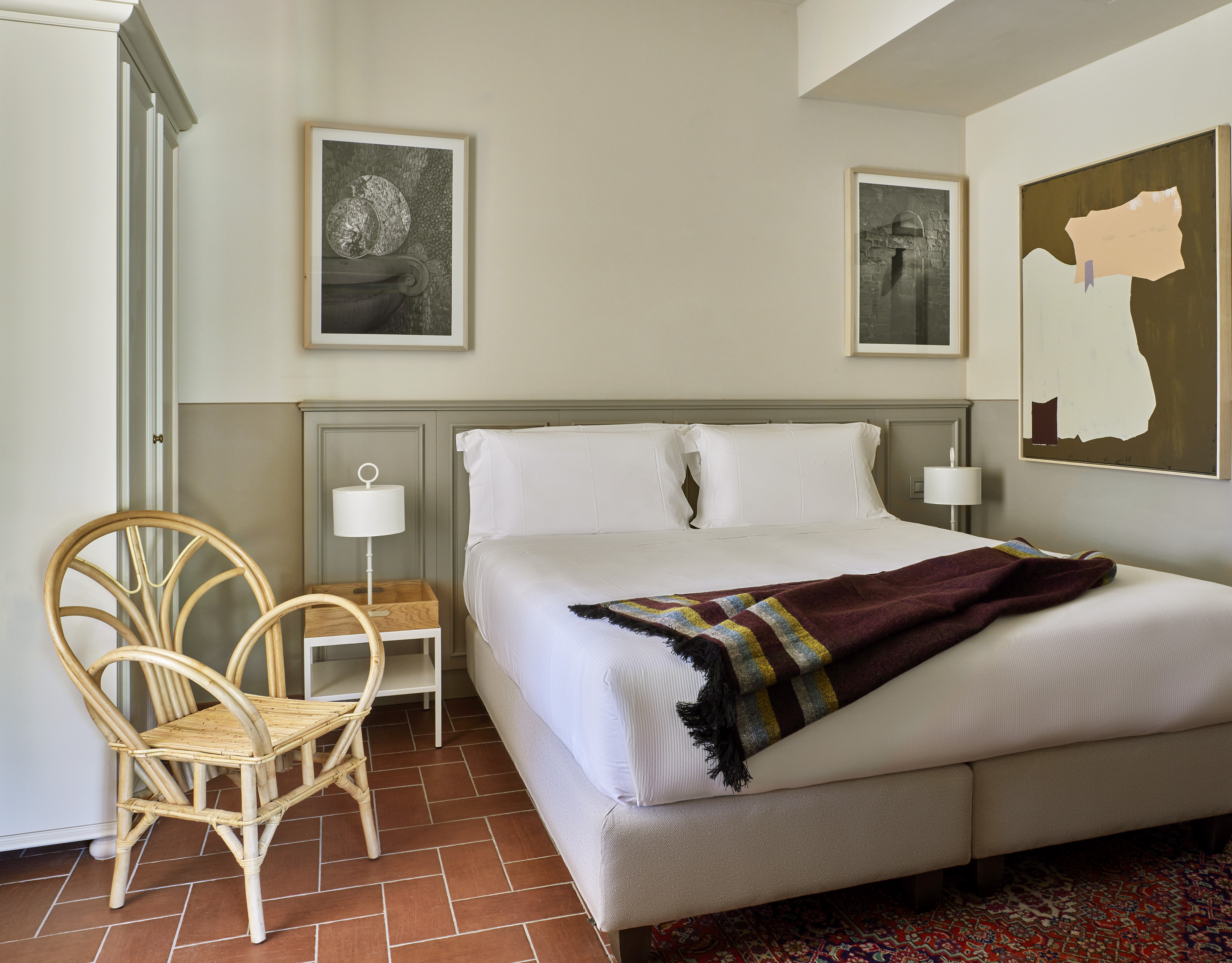 Cozy bedroom with white bed, striped blanket, rattan chair, and terracotta tiles.