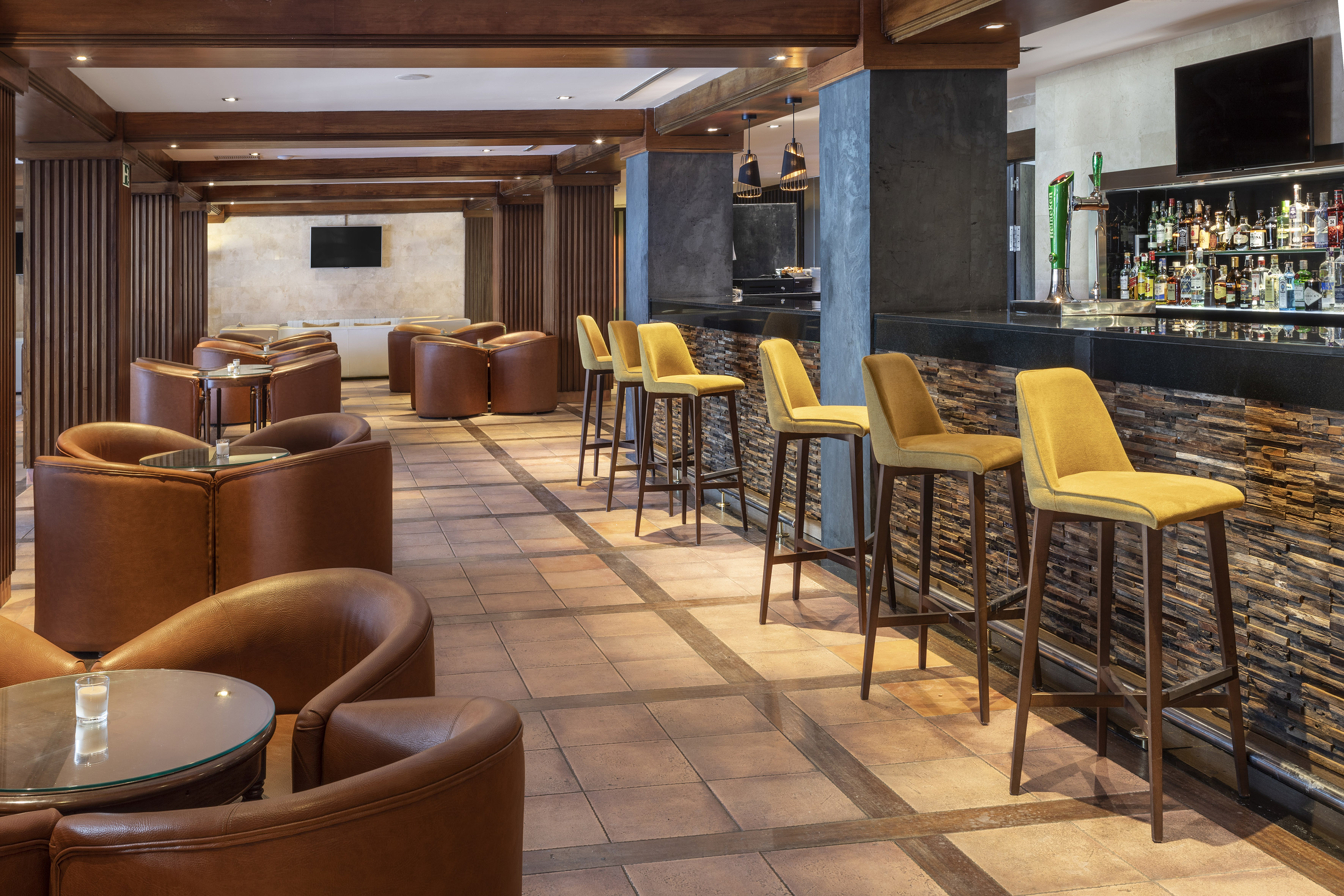 Elegant hotel bar lounge with yellow stools and brown leather seating.
