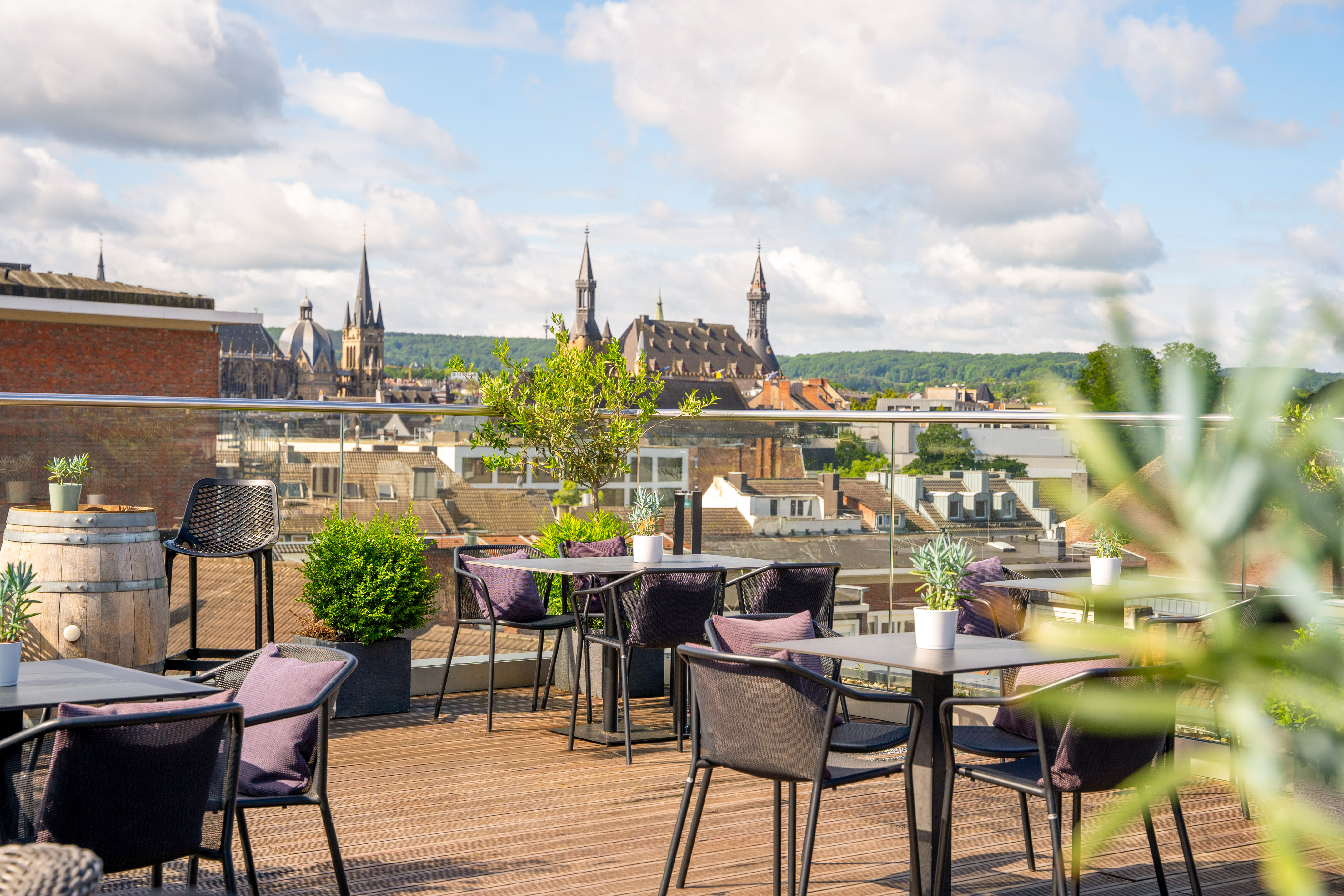 Rooftop terrace with outdoor seating, city skyline, and Aachen Cathedral view.