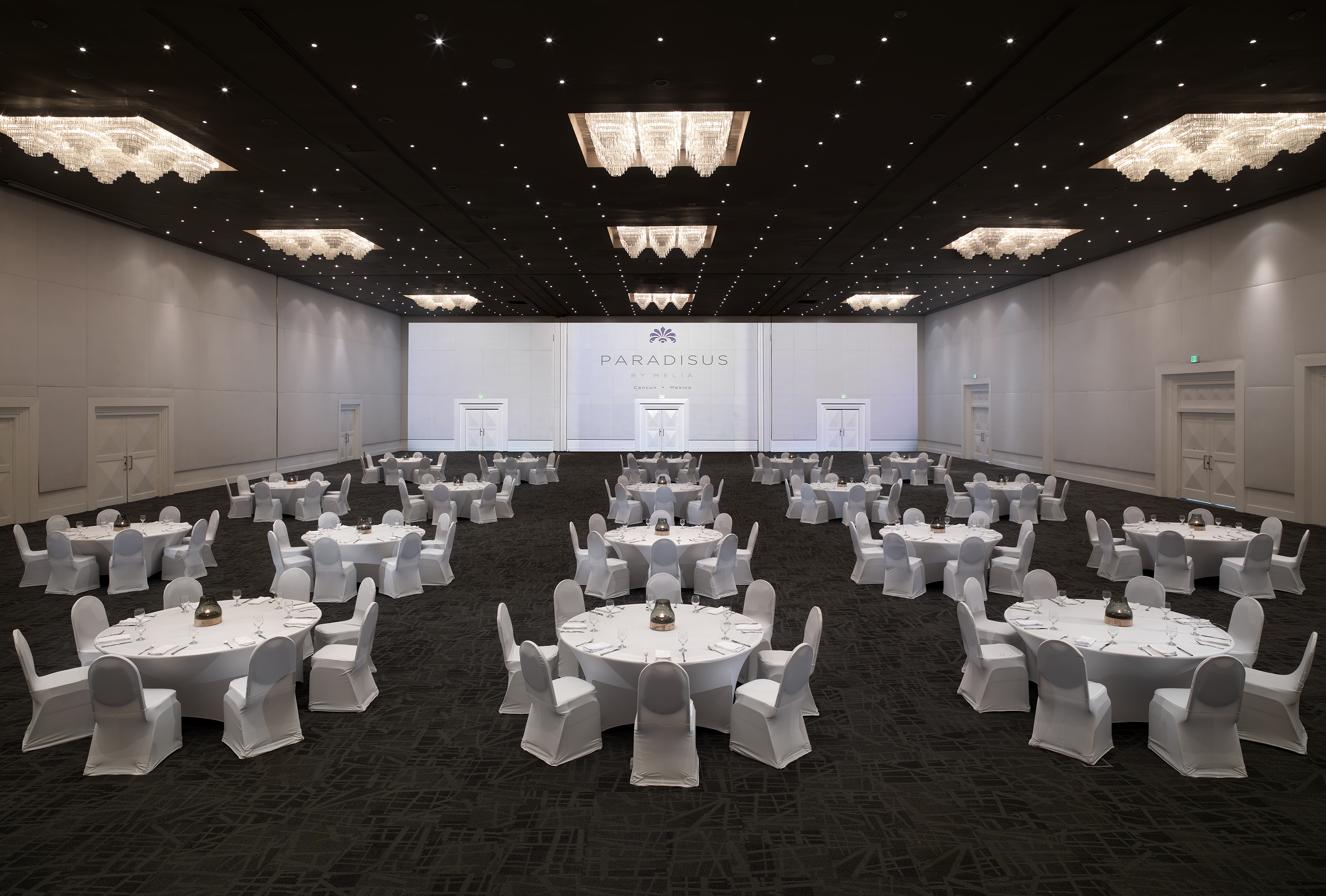Elegant Paradisus ballroom, round tables set for a banquet with sparkling chandeliers.