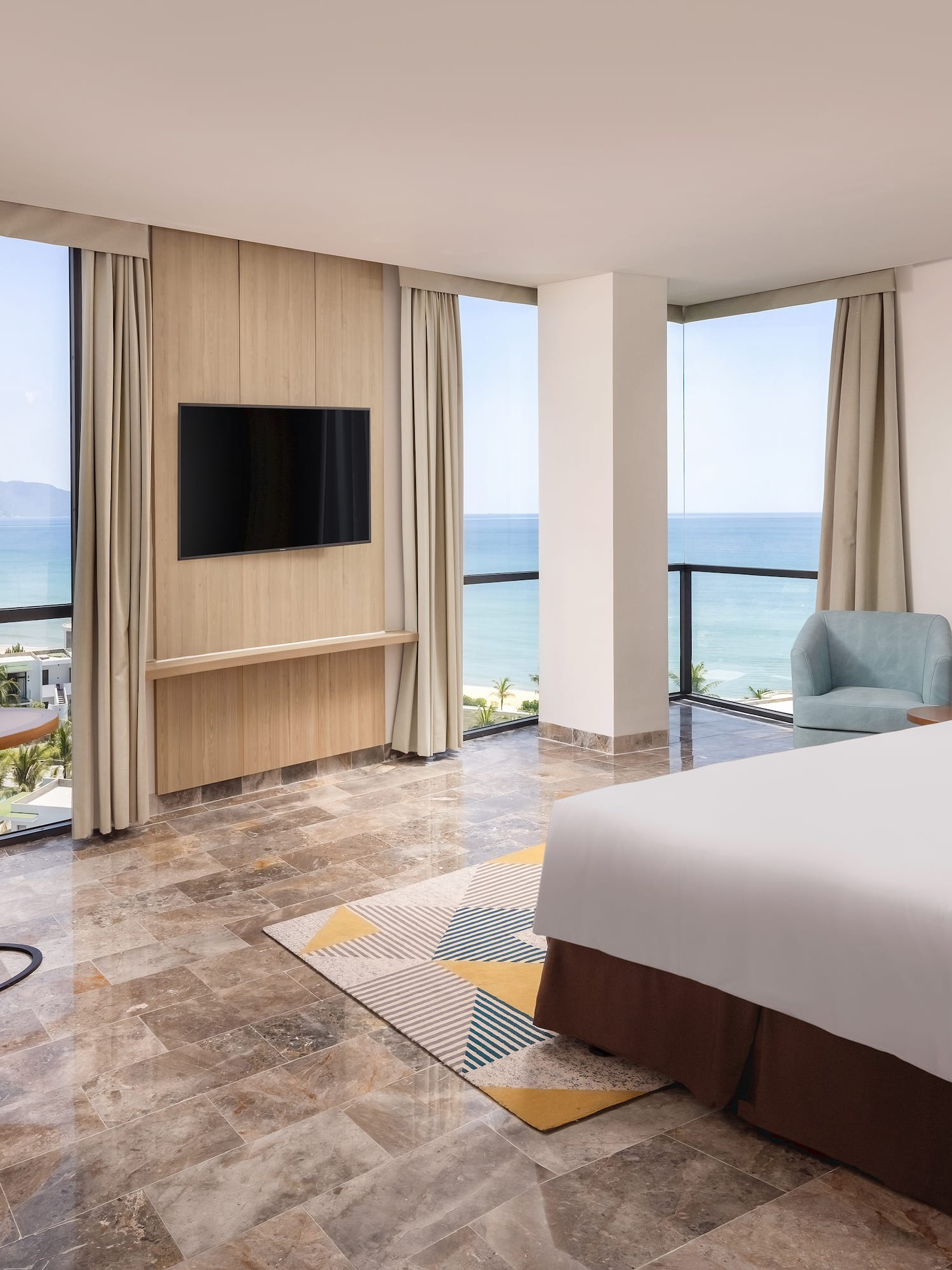 Beachfront hotel room with ocean view, king bed, TV, and modern furnishings.
