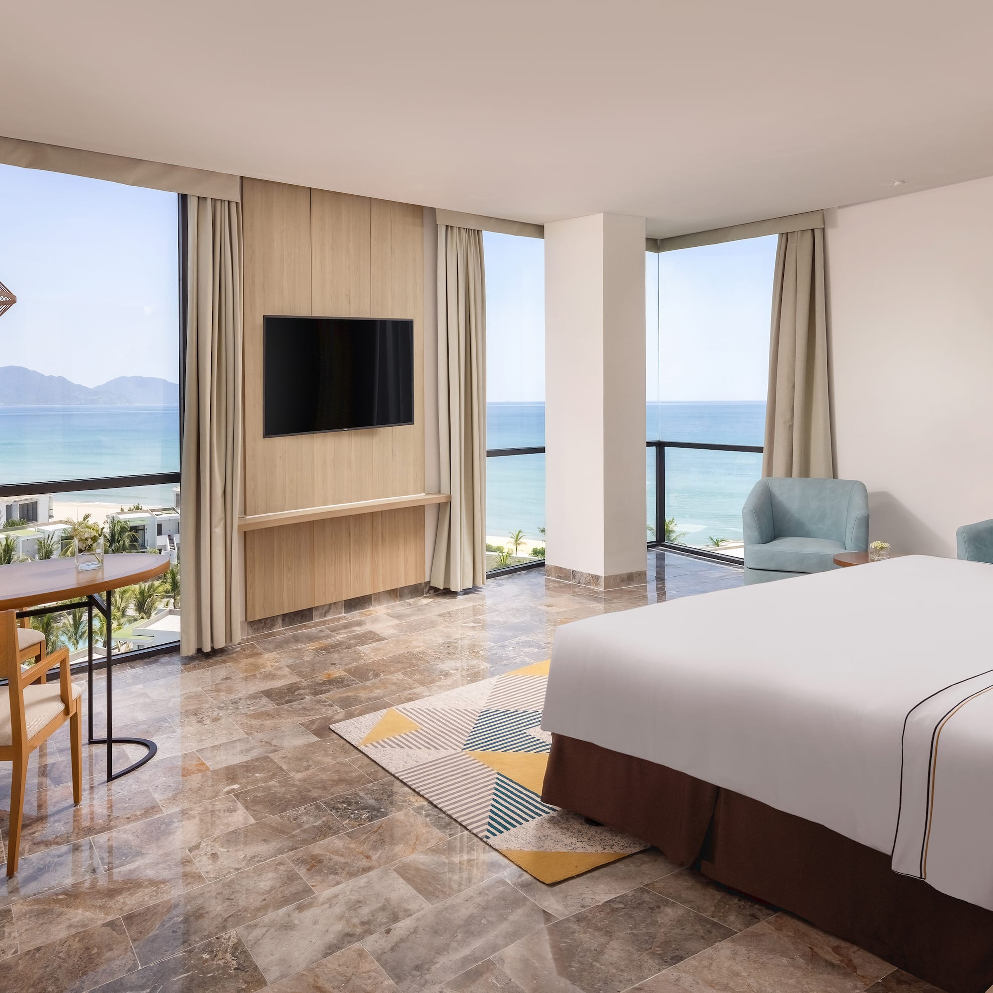 a room with a bed and a table and chairs by the ocean