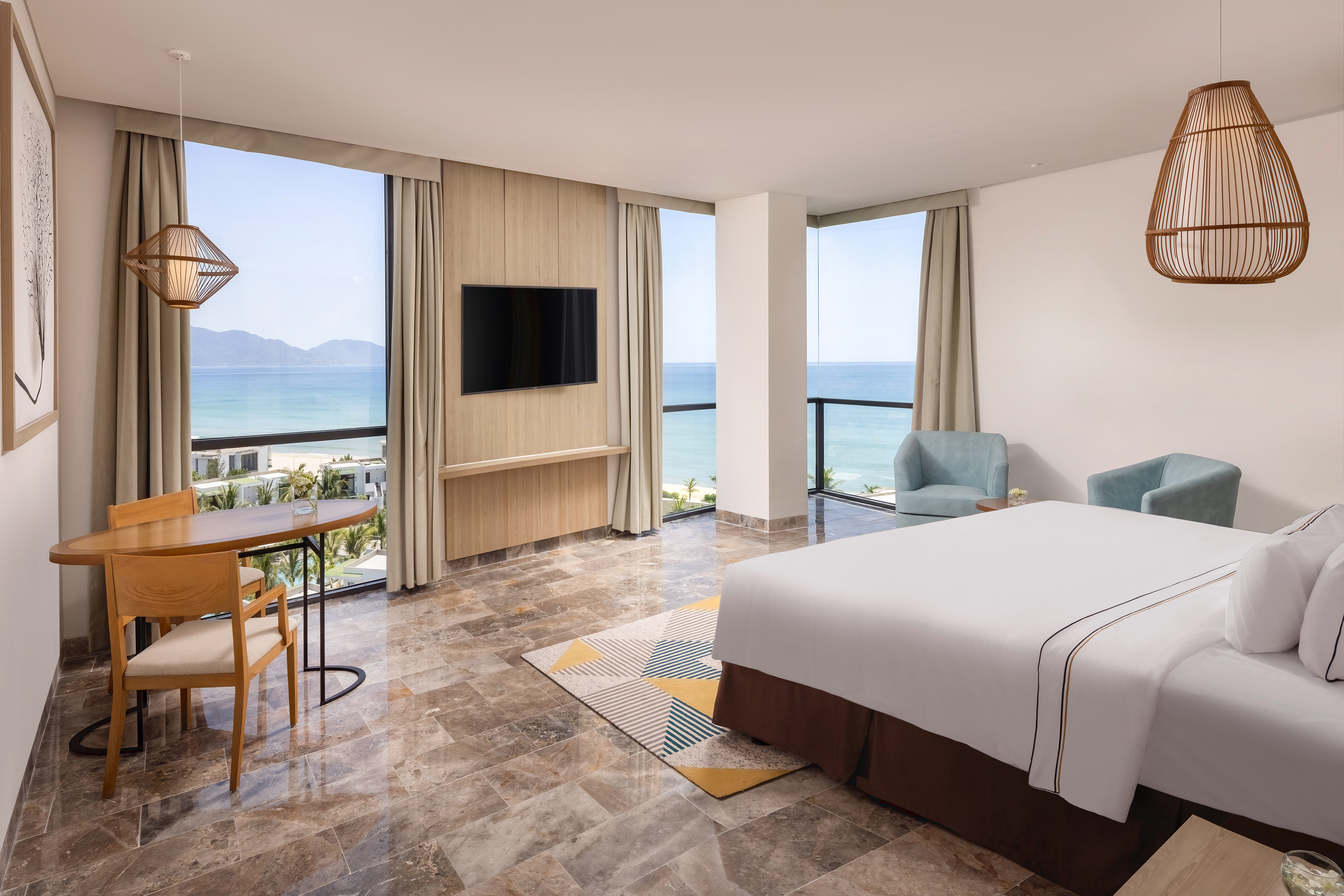 Beachfront hotel room with ocean view, king bed, TV, and modern furnishings.