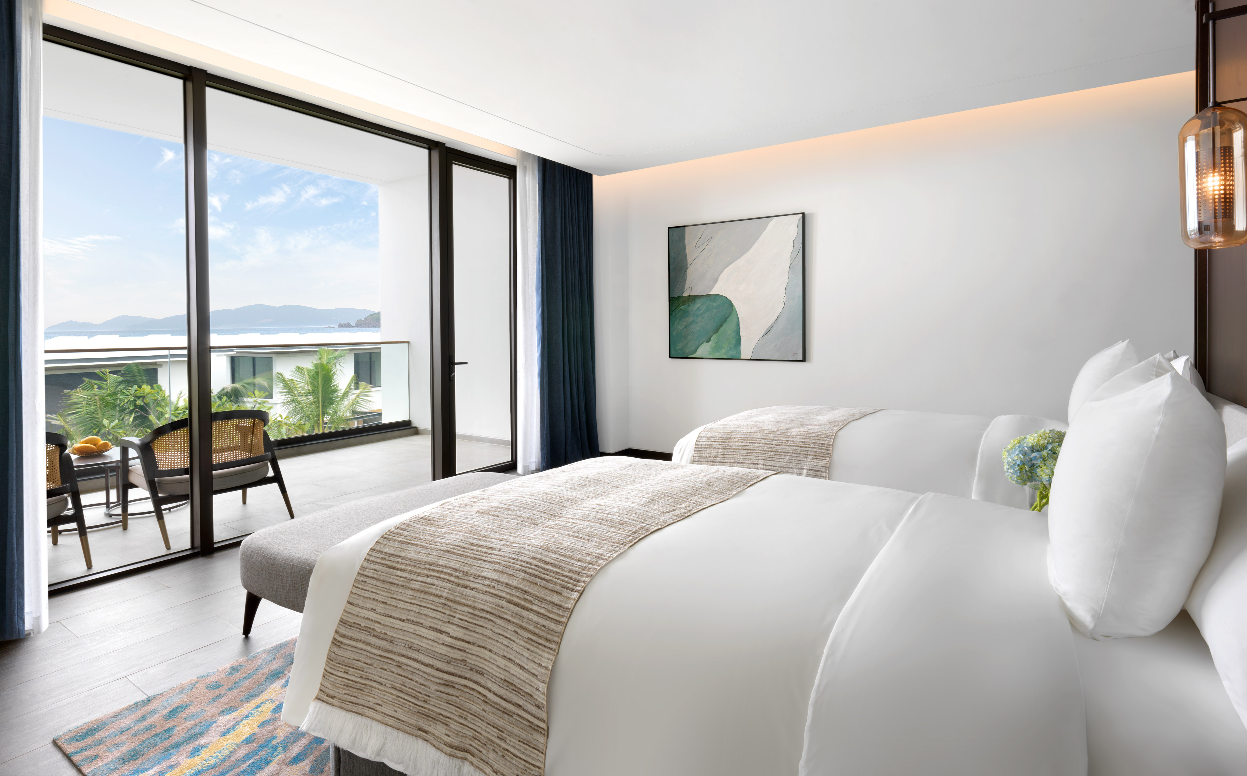 Modern hotel bedroom with ocean view balcony, two beds, and contemporary decor.