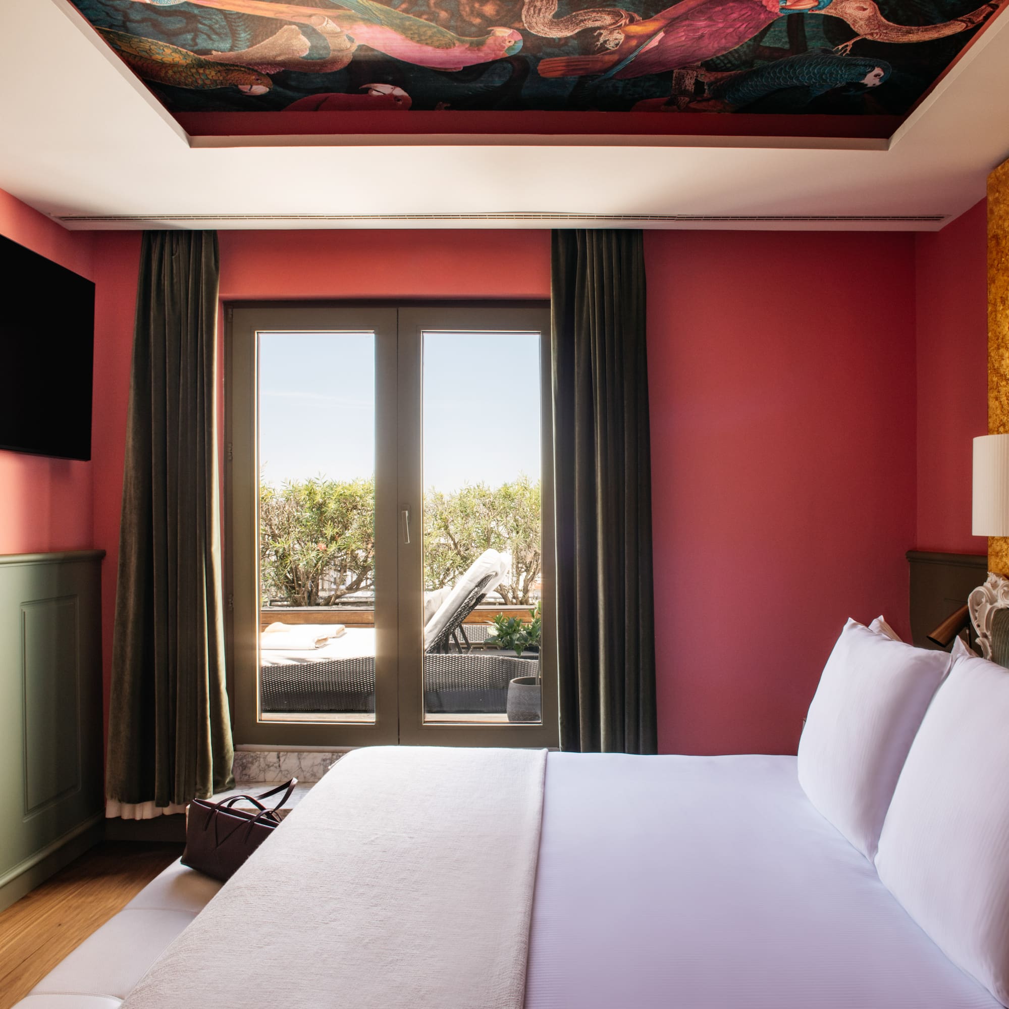 a bed with white sheets and a red wall with a painting on the ceiling