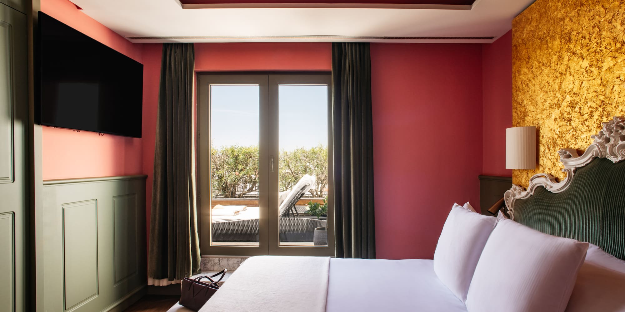 a bed with white sheets and a red wall with a painting on the ceiling