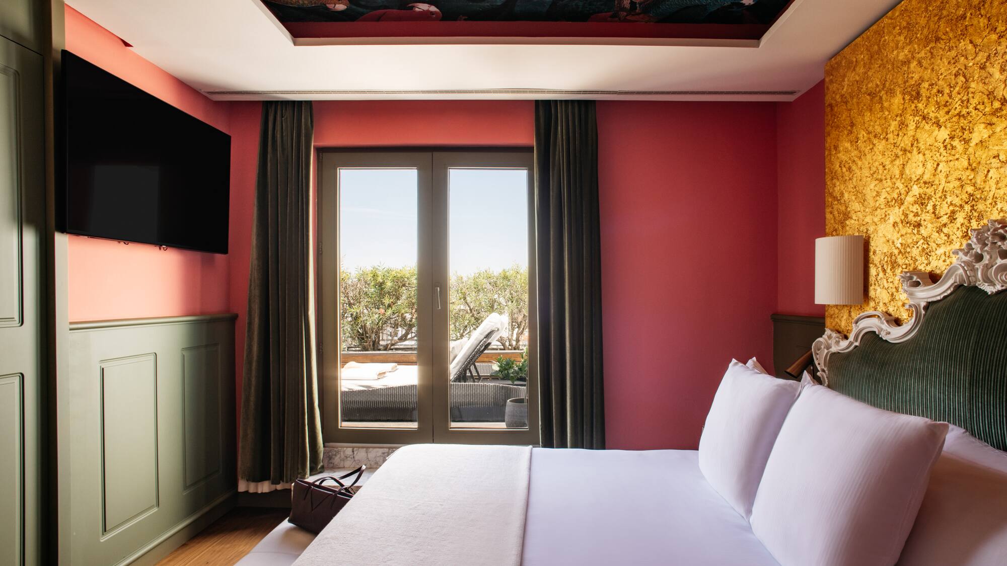 a bed with white sheets and a red wall with a painting on the ceiling