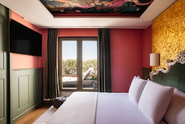 a bed with white sheets and a red wall with a painting on the ceiling