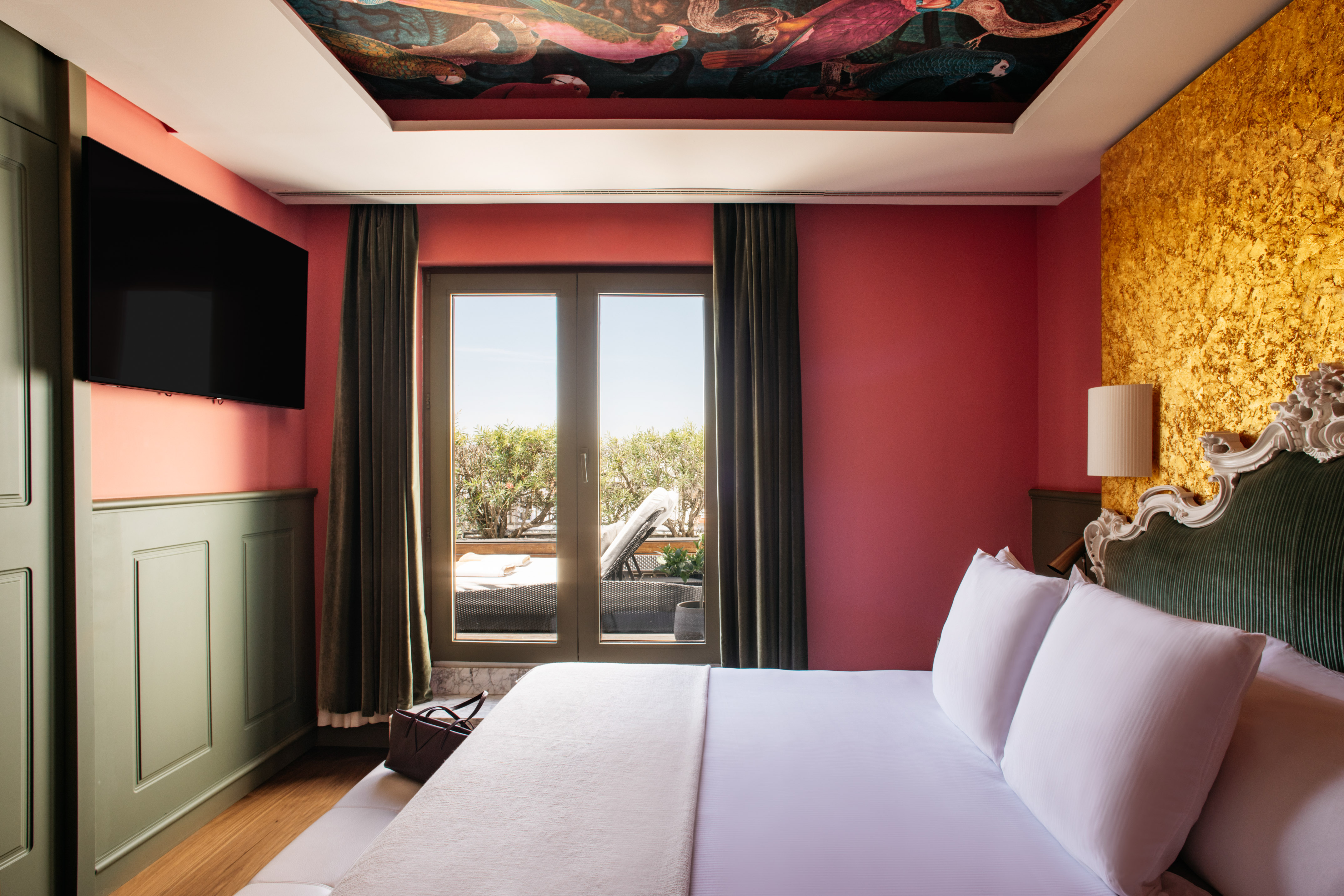 a bed with white sheets and a red wall with a painting on the ceiling