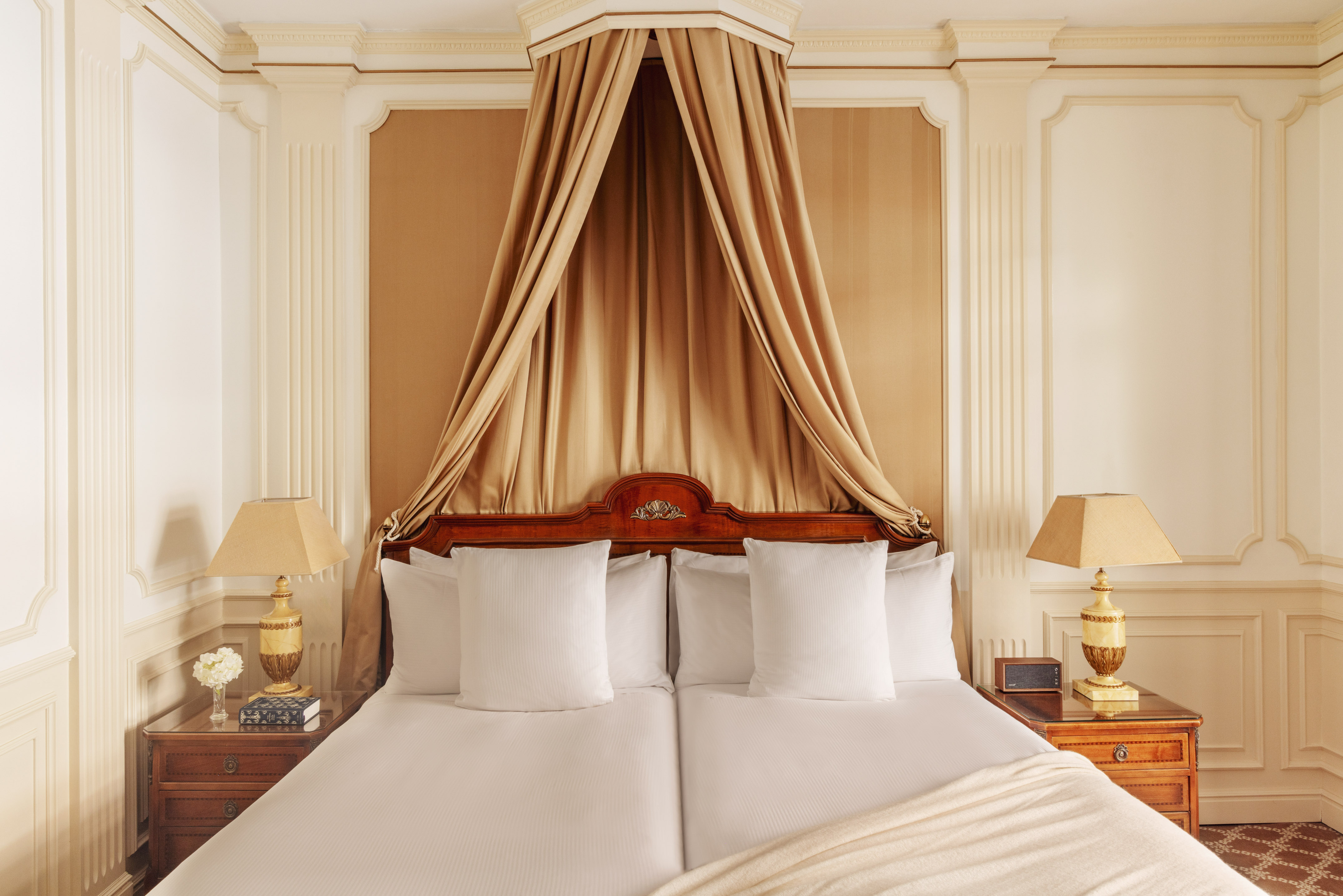 Elegant luxury hotel bedroom with beige canopy bed and classic decor.