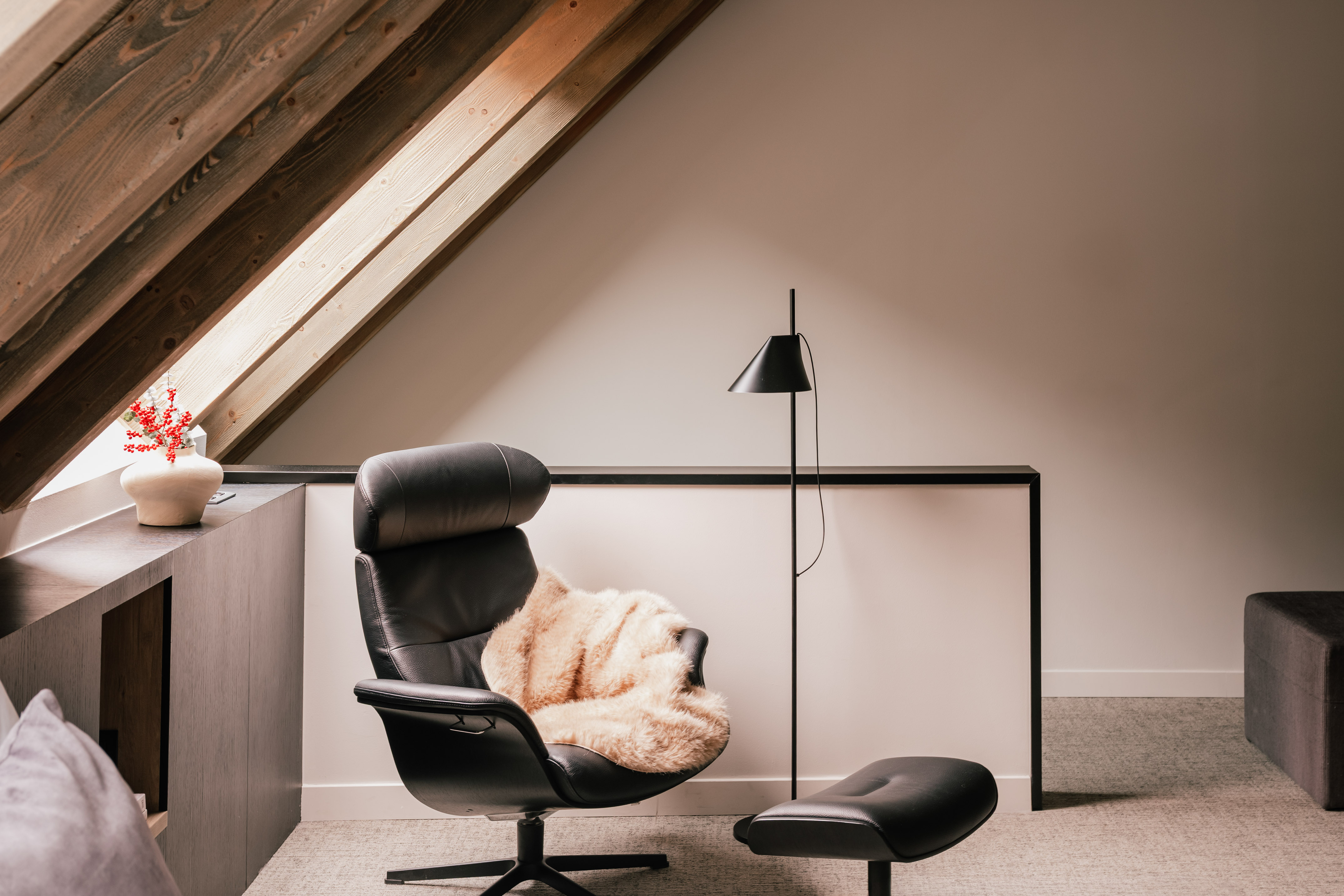 Modern black leather armchair and ottoman under slanted wooden attic beams.