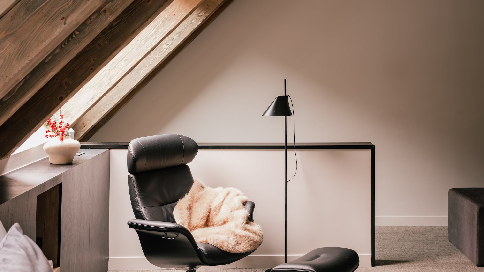 Modern black leather armchair and ottoman under slanted wooden attic beams.
