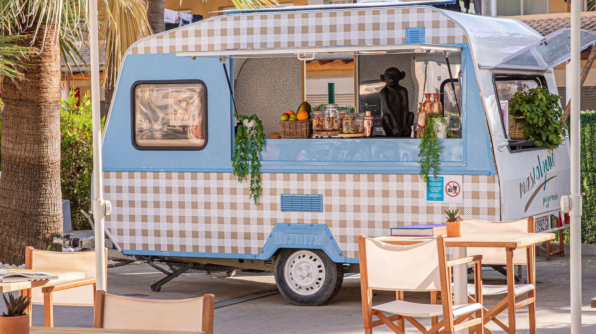 Blue checkered food truck at an outdoor tropical cafe with patio seating.