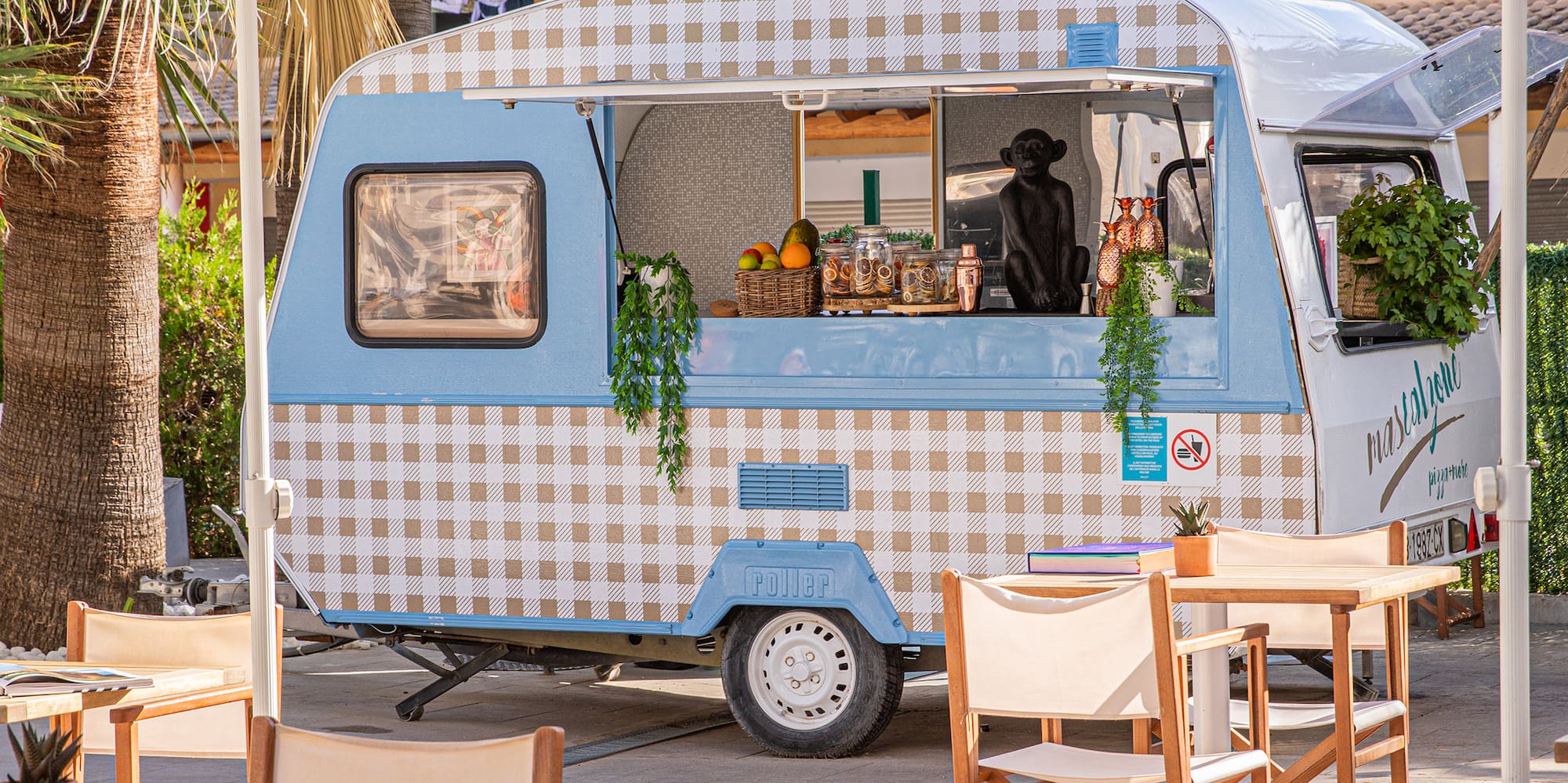 Blue checkered food truck at an outdoor tropical cafe with patio seating.