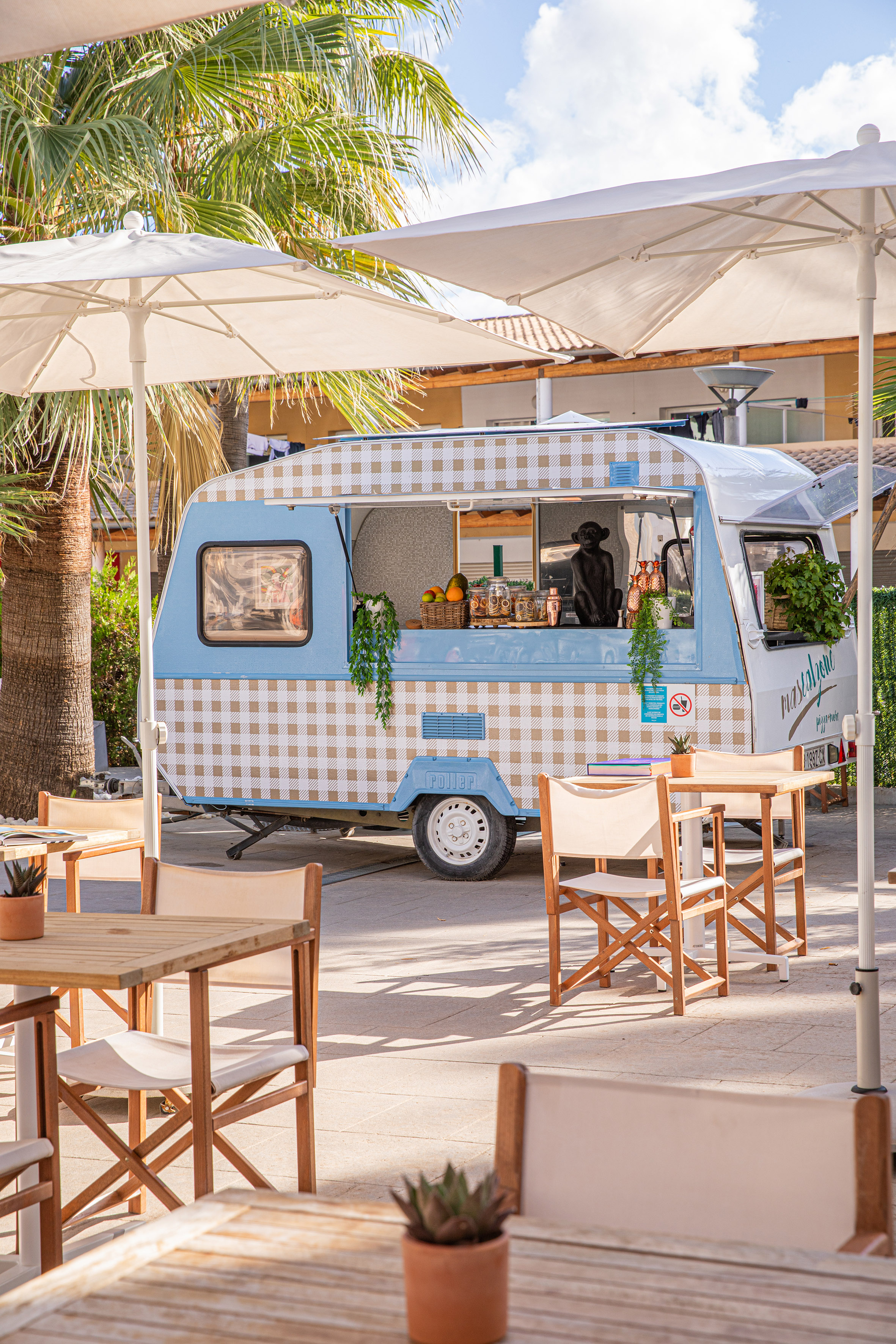 Blue checkered food truck at an outdoor tropical cafe with patio seating.