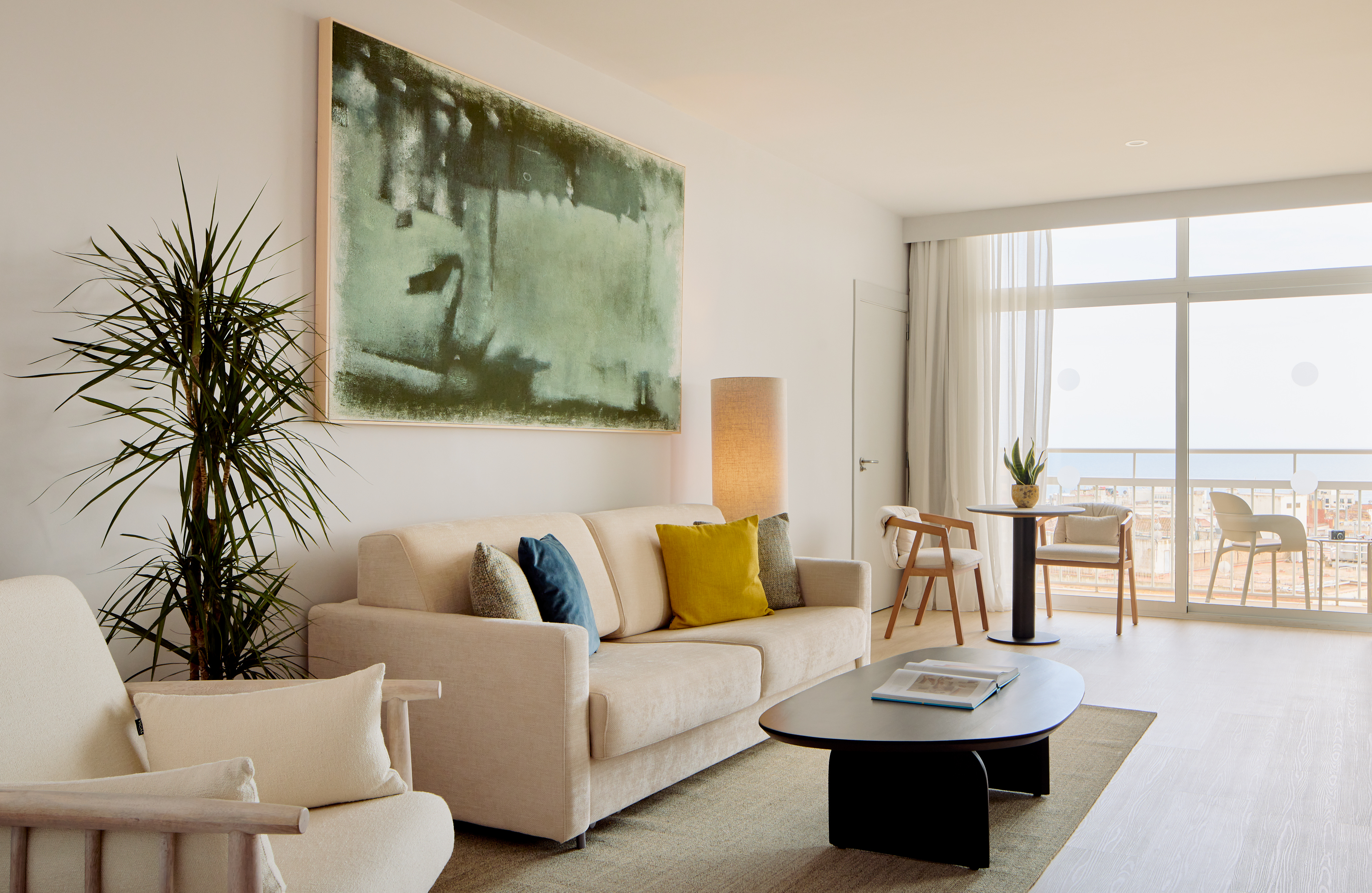 Modern living room with light sofa, abstract green art, and city view balcony.