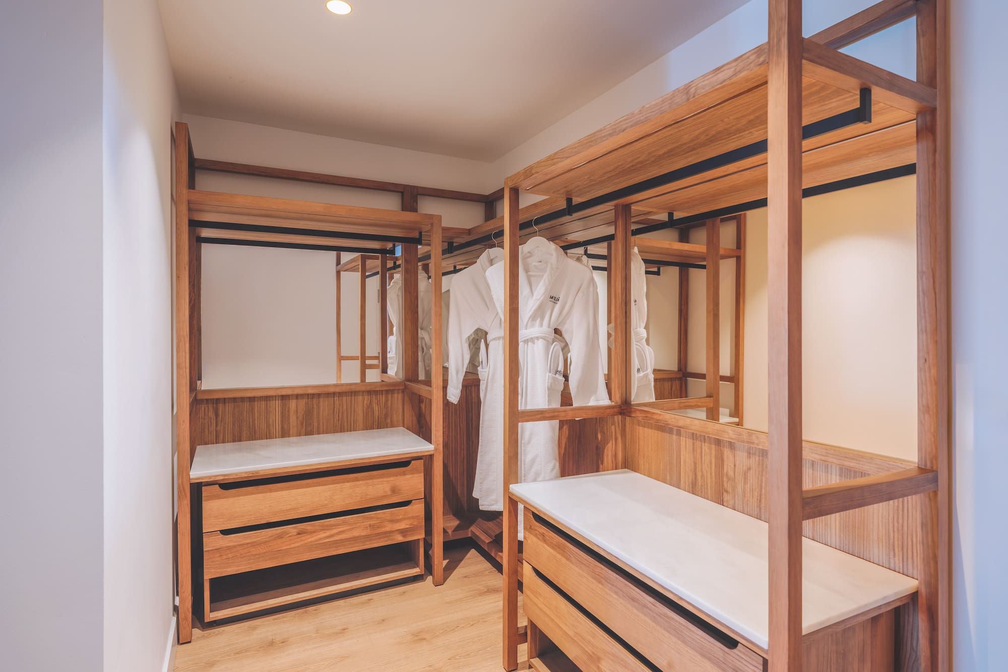 Wood walk-in closet with white bathrobes, storage drawers, and mirrors.