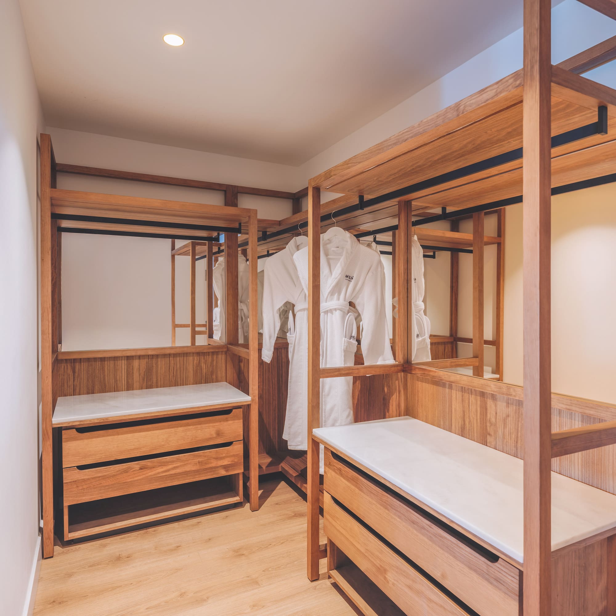 Wood walk-in closet with white bathrobes, storage drawers, and mirrors.