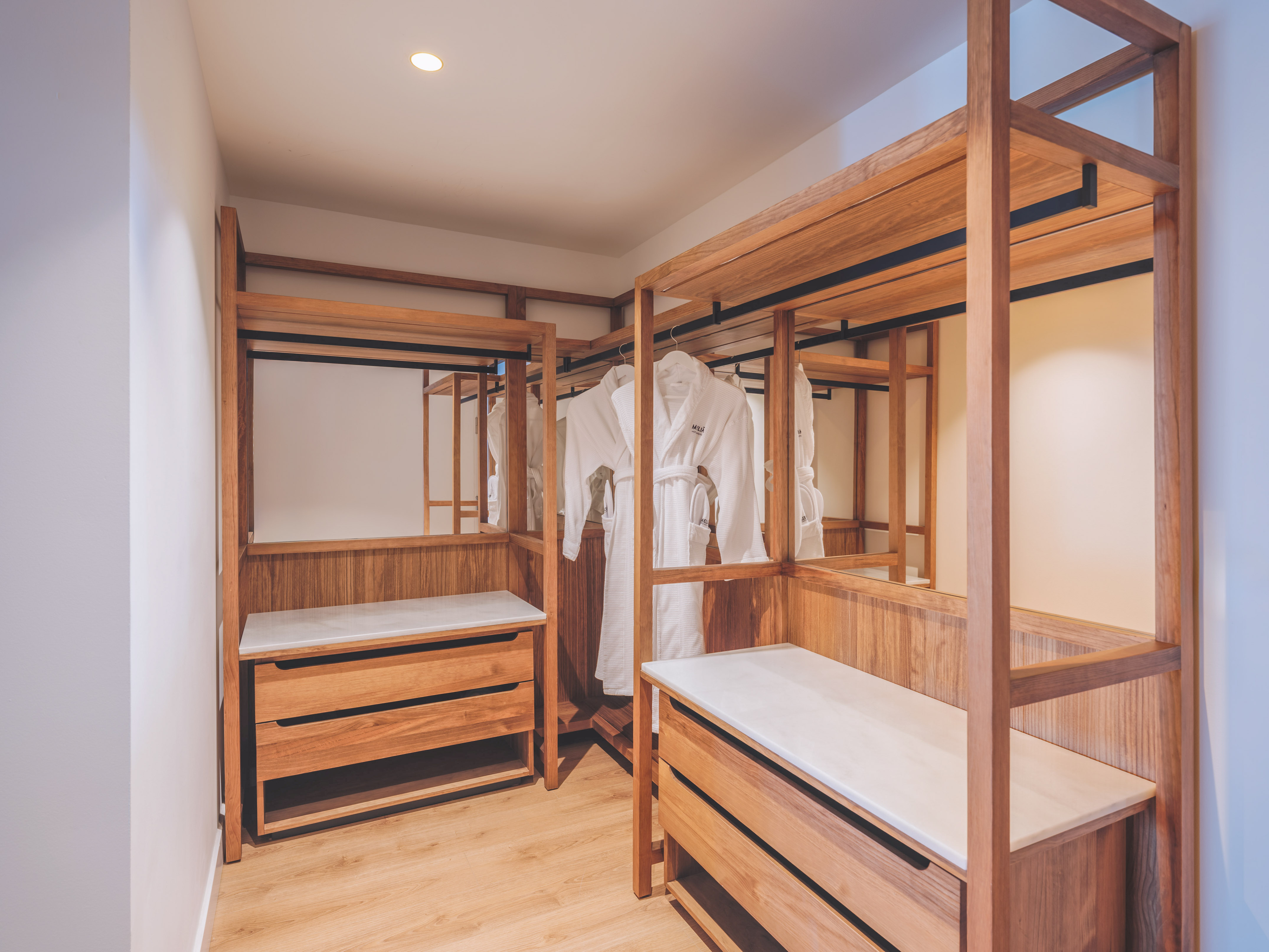 Wood walk-in closet with white bathrobes, storage drawers, and mirrors.