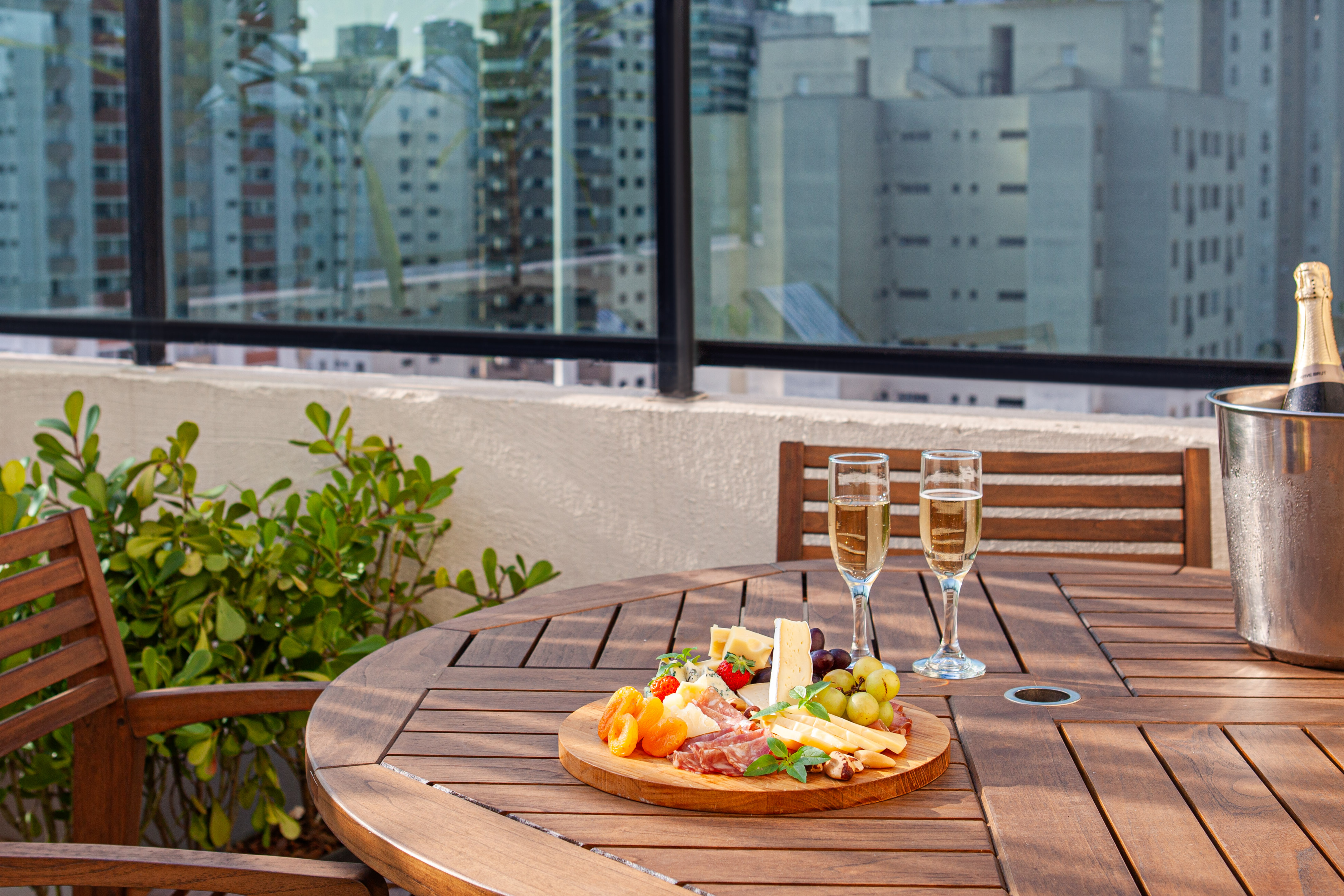 Outdoor table with champagne, cheese board, charcuterie, and city view.