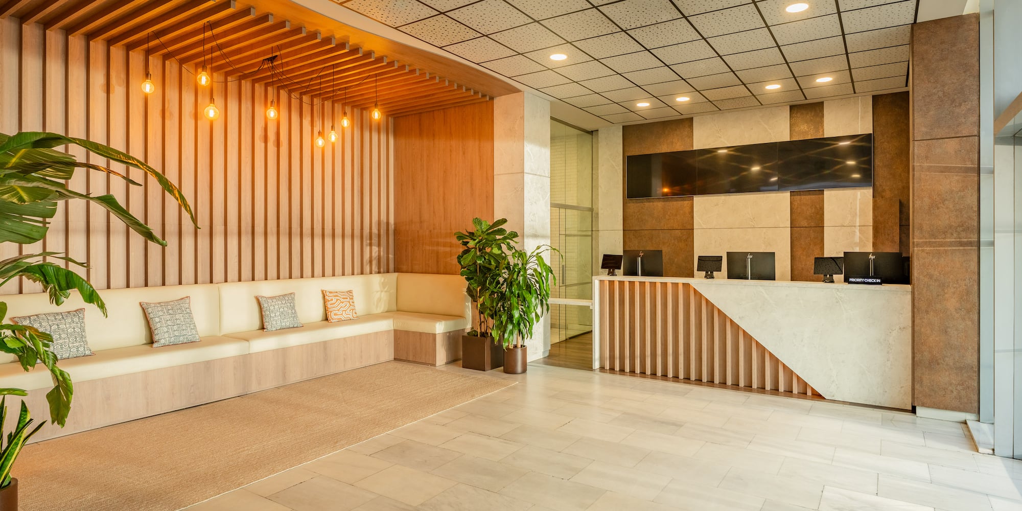 Modern hotel lobby with reception desk, sofa, wooden accents, and marble floor.