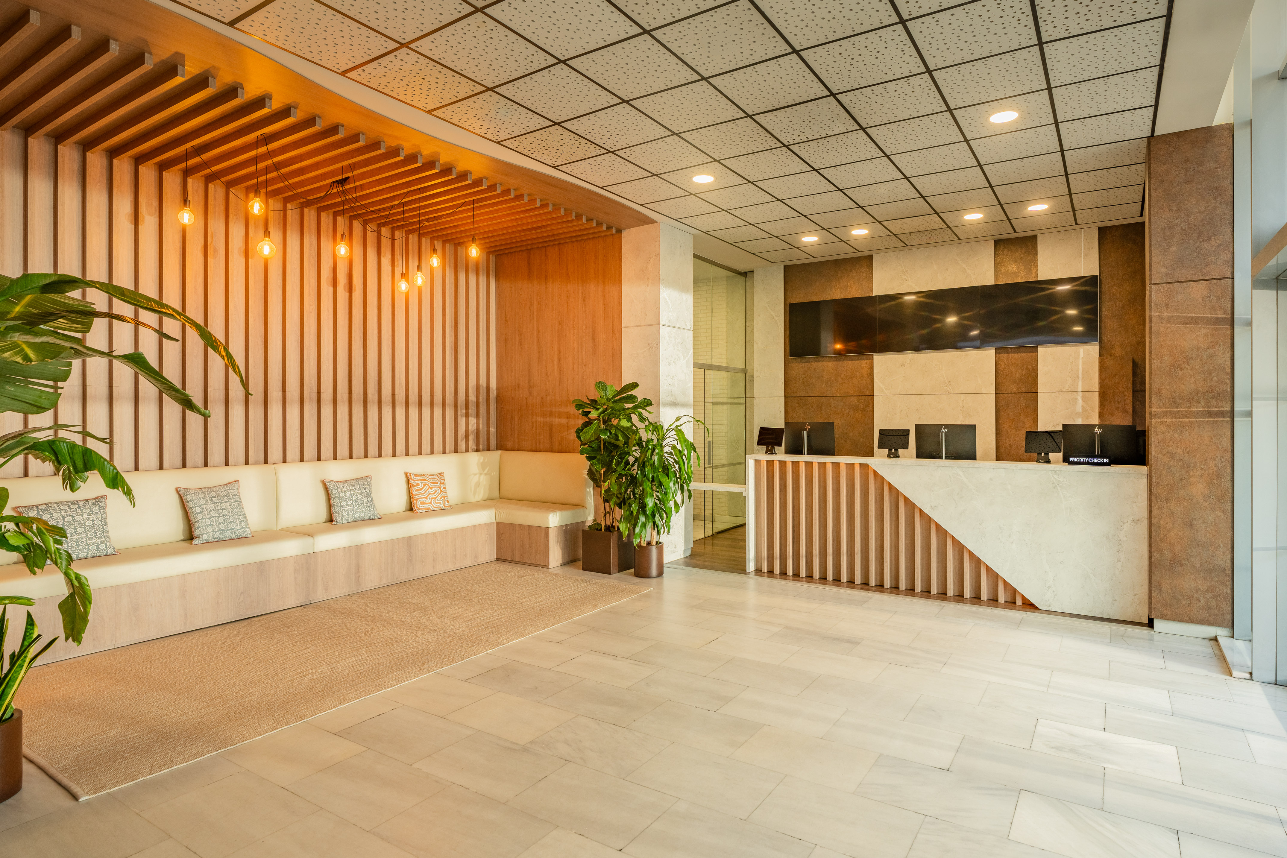 Modern hotel lobby with reception desk, sofa, wooden accents, and marble floor.