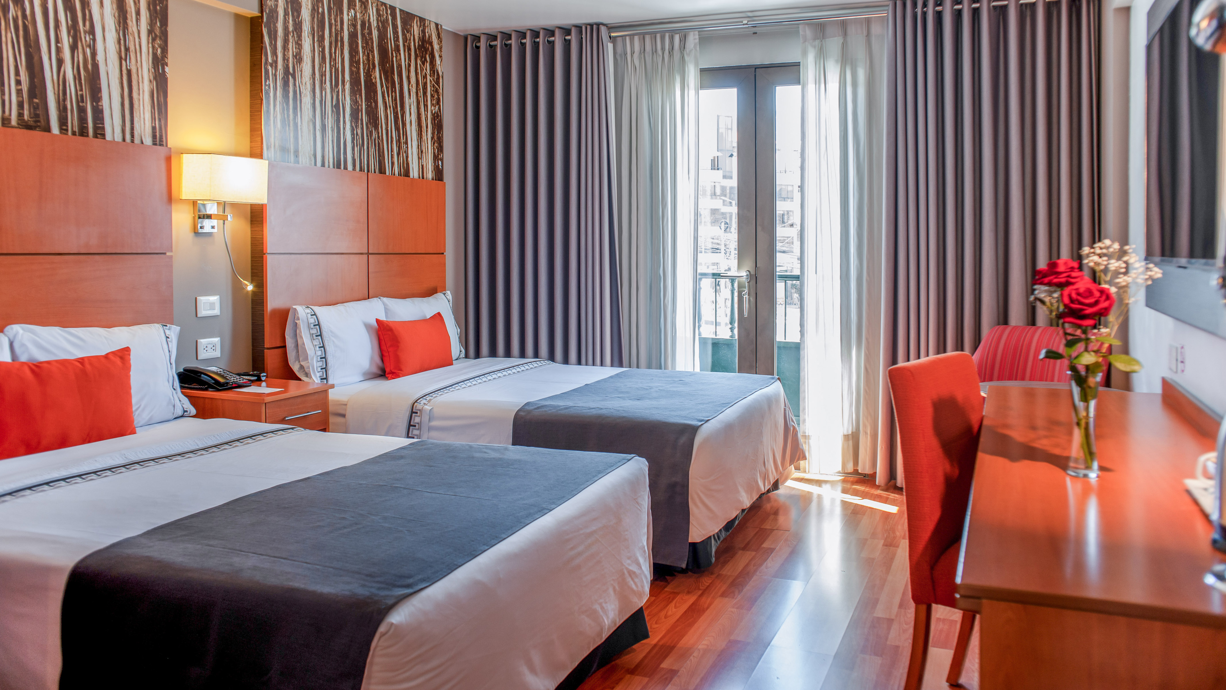 Modern twin bed hotel room with orange accents, wood, and sunny window.