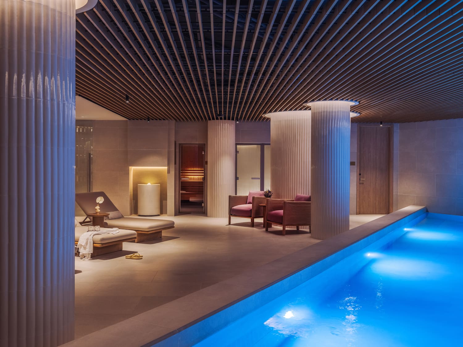 a pool with chairs and a lounge chair in a room with columns