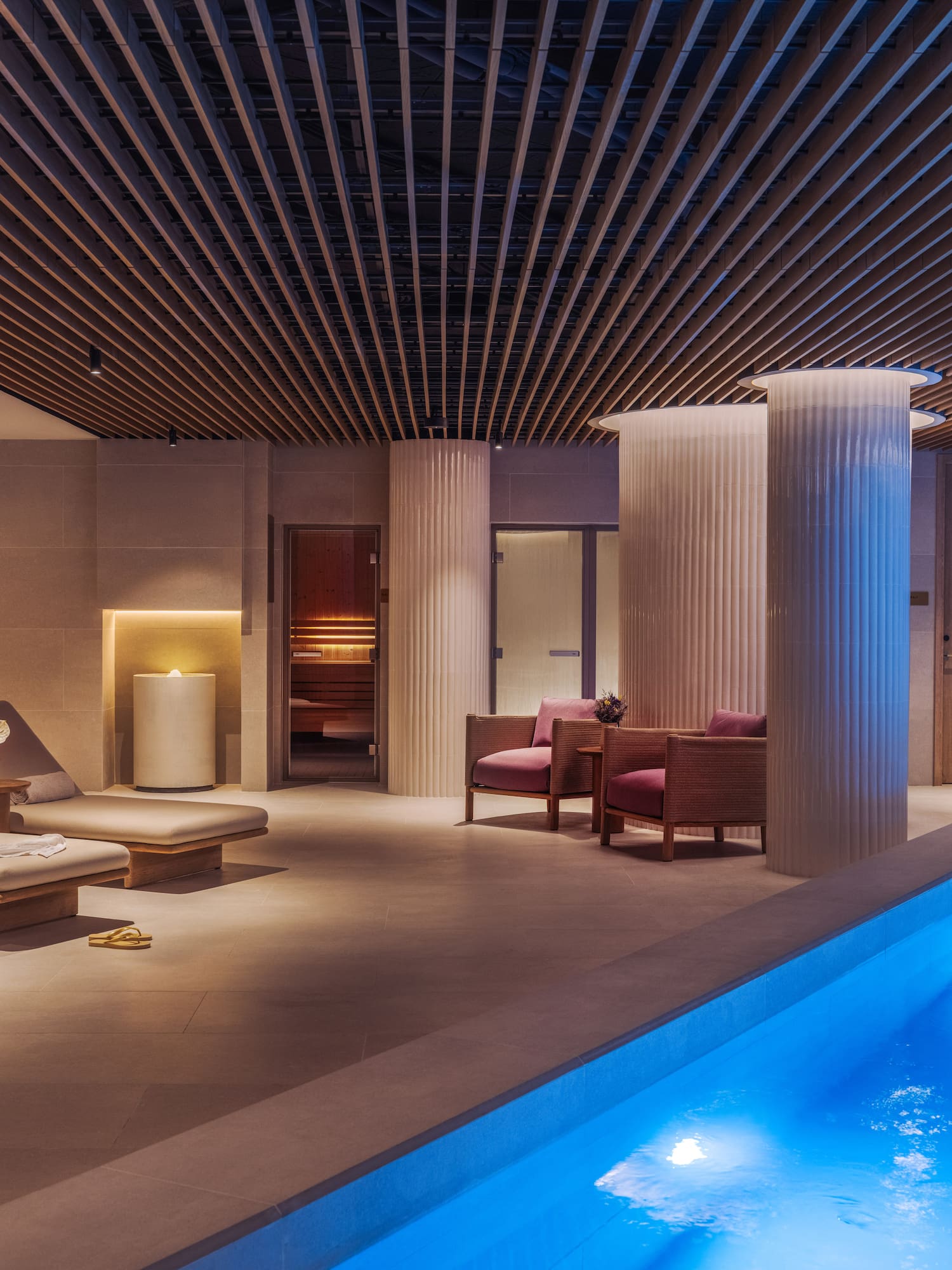 a pool with chairs and a lounge chair in a room with columns