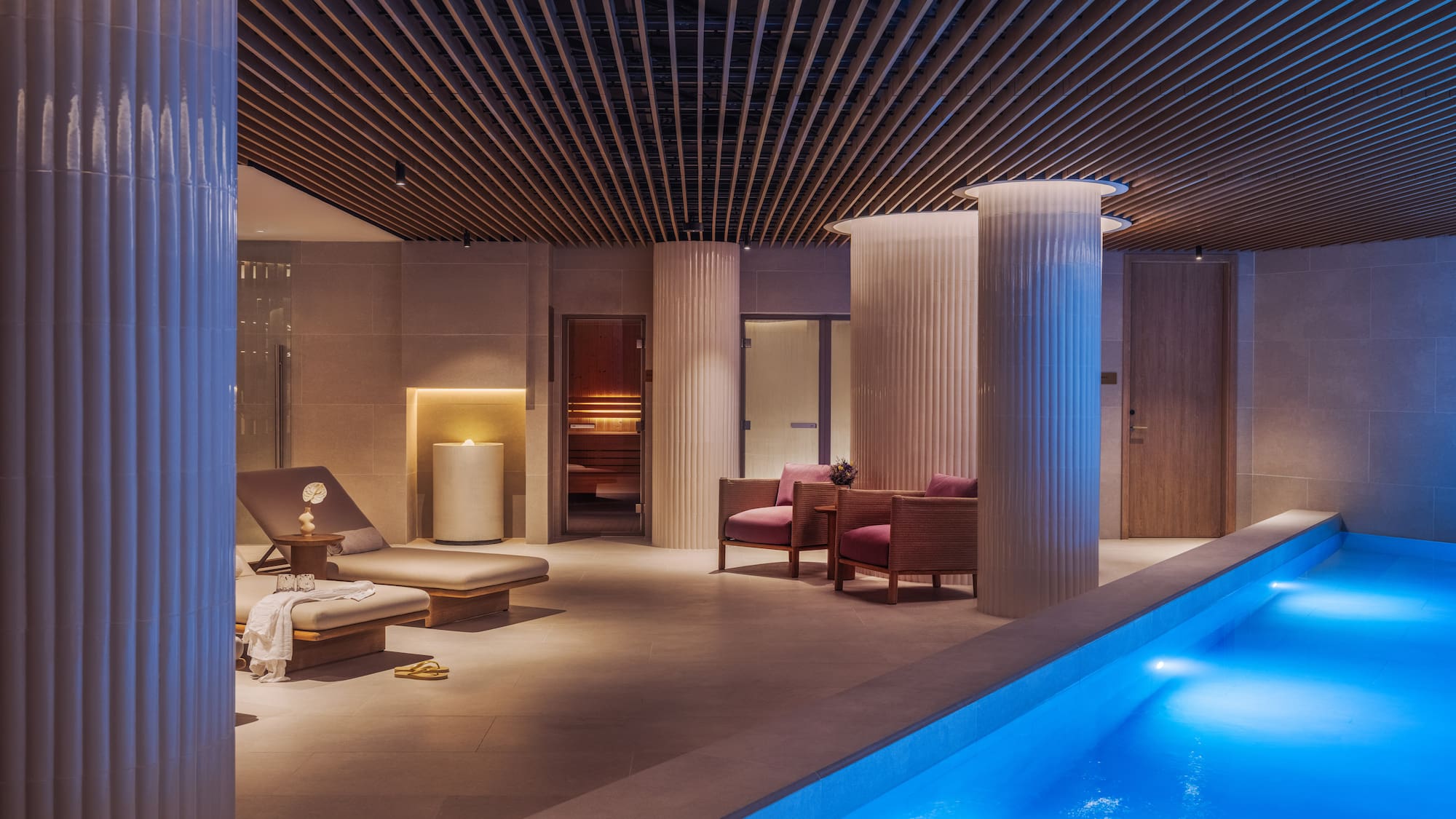 a pool with chairs and a lounge chair in a room with columns