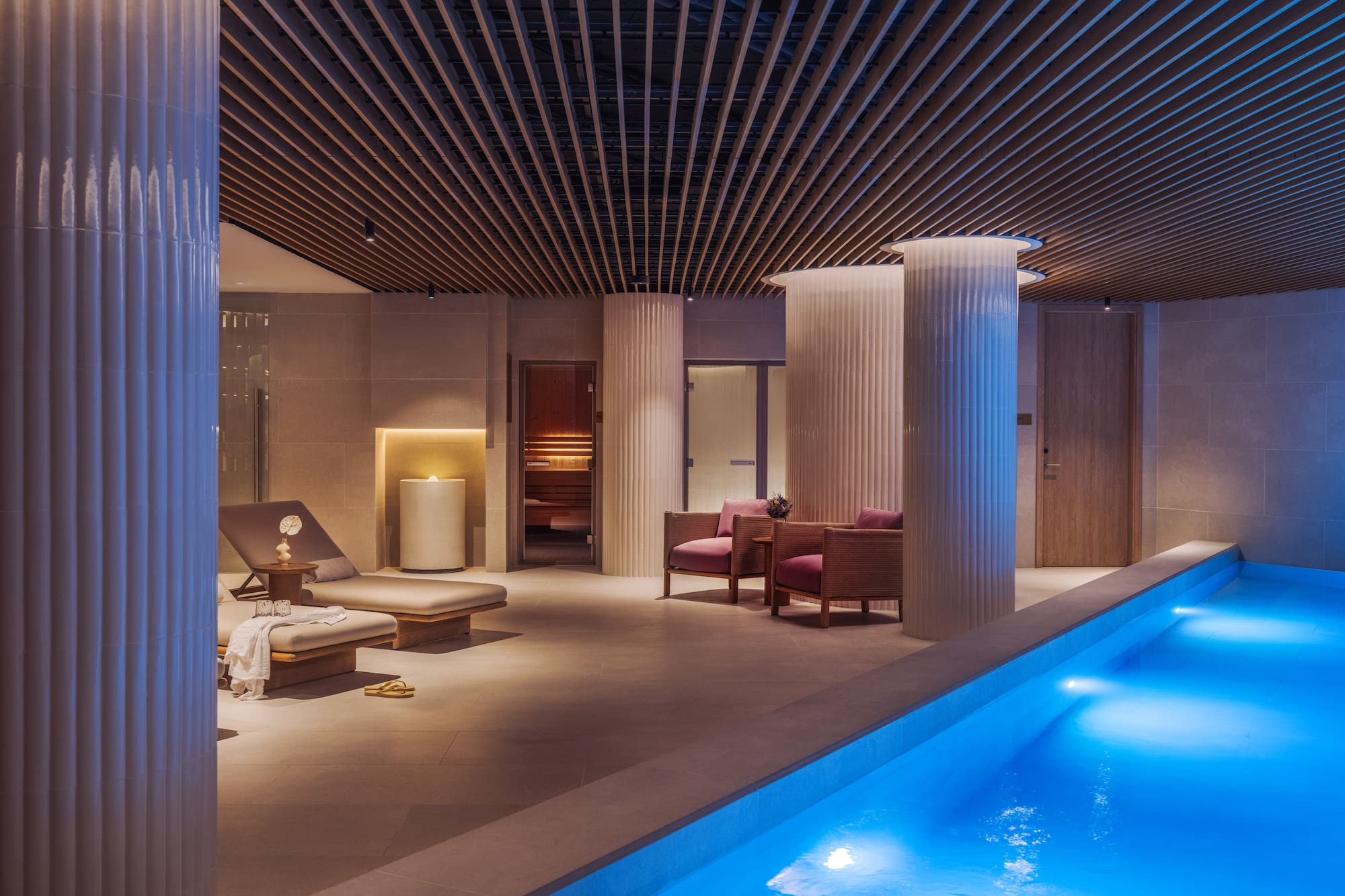 a pool with chairs and a lounge chair in a room with columns