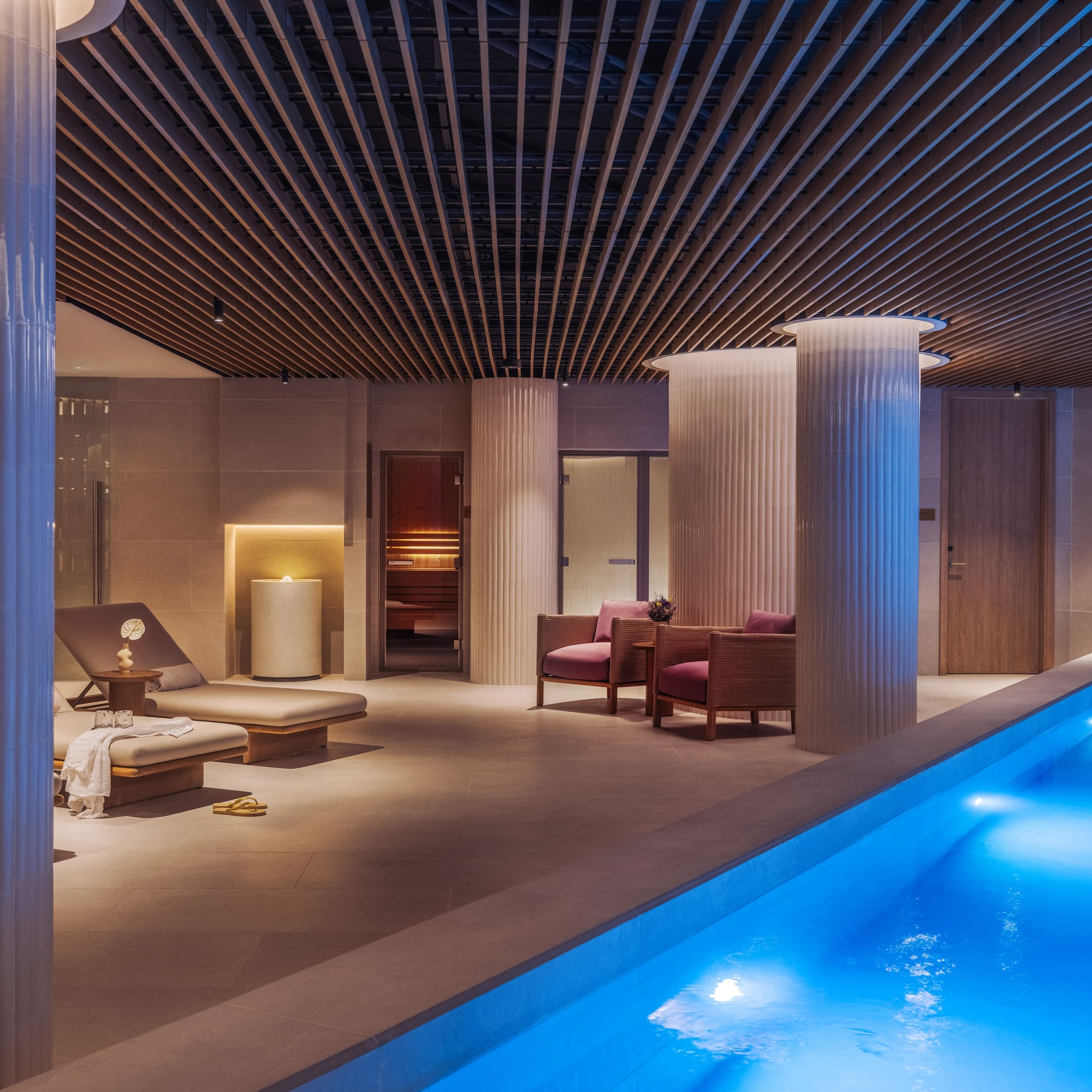 a pool with chairs and a lounge chair in a room with columns