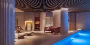 a pool with chairs and a lounge chair in a room with columns