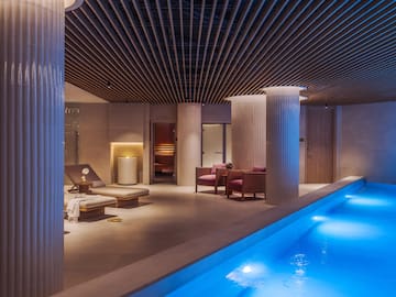 a pool with chairs and a lounge chair in a room with columns