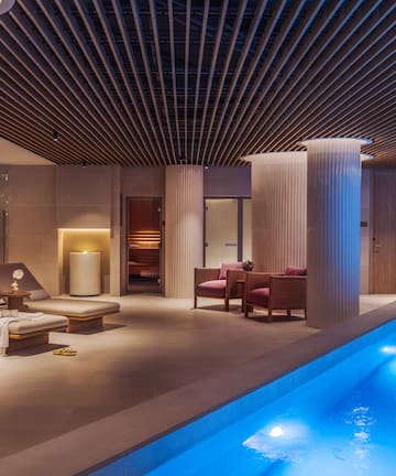 a pool with chairs and a lounge chair in a room with columns