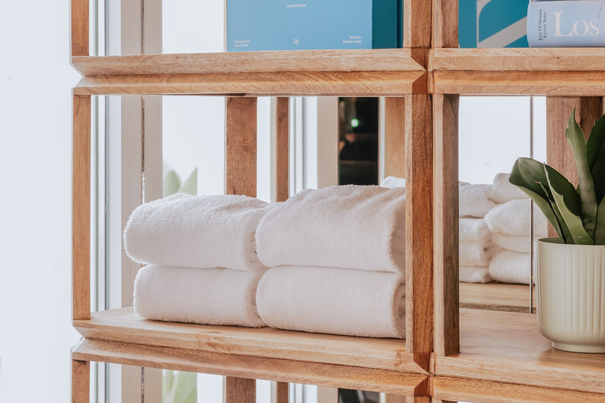 Wooden shelving unit with Ibiza book, folded white towels, and storage baskets.