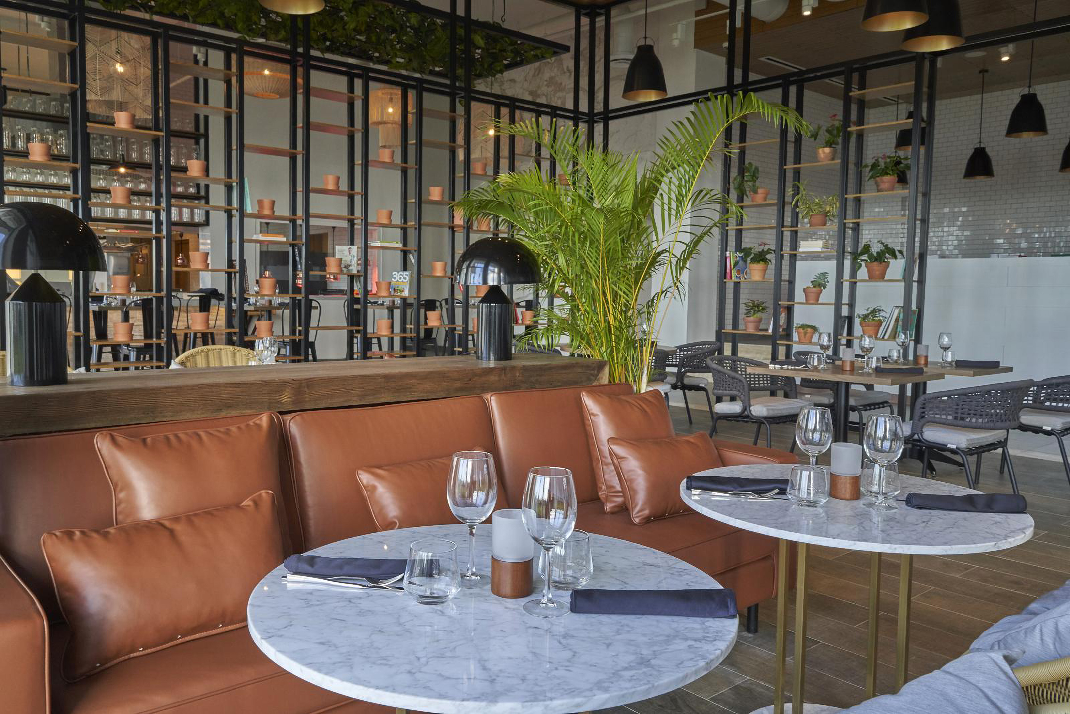 Modern restaurant dining with leather banquette, marble tables, and lush plants.