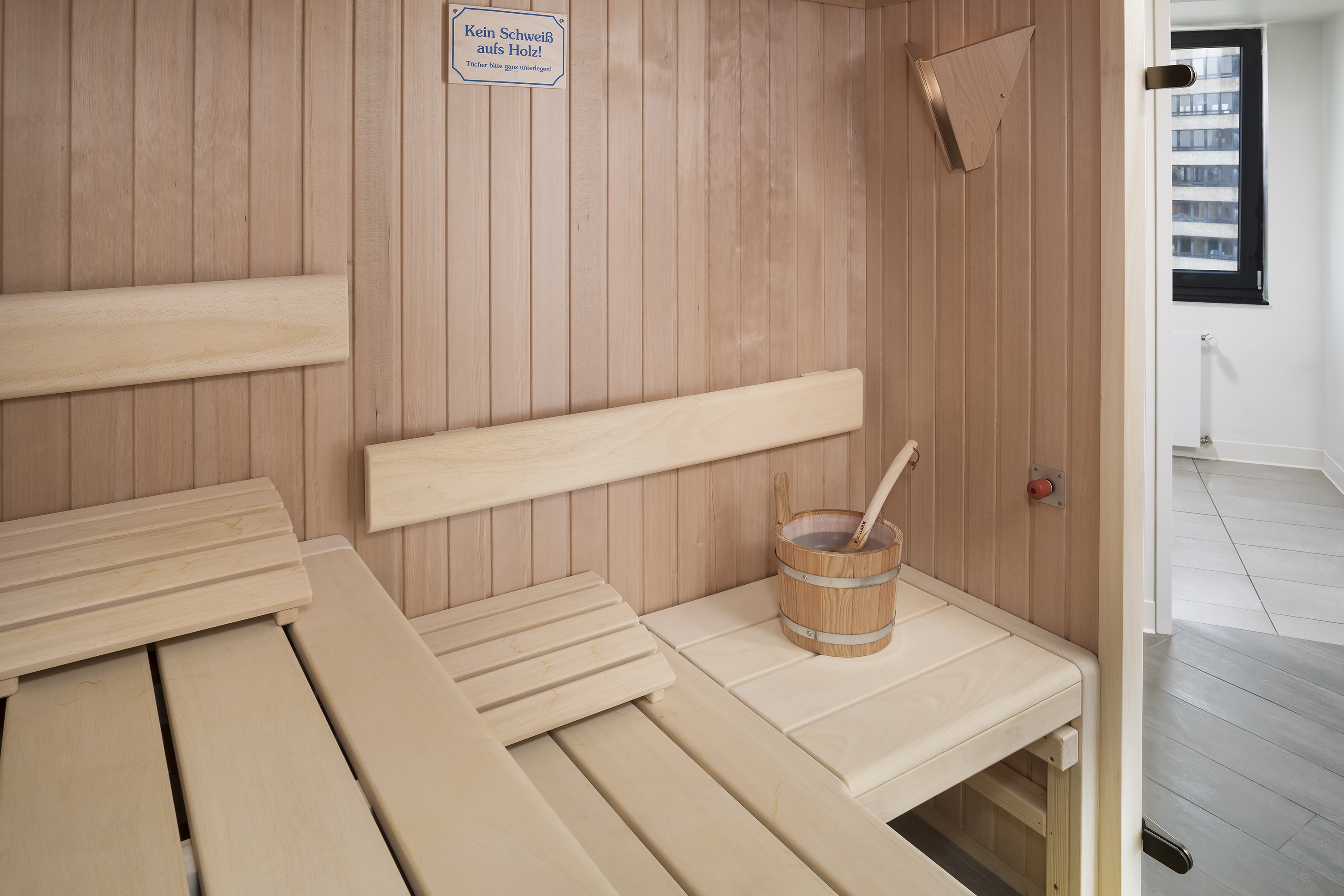 Light wood sauna interior with clean benches, bucket, and ladle.