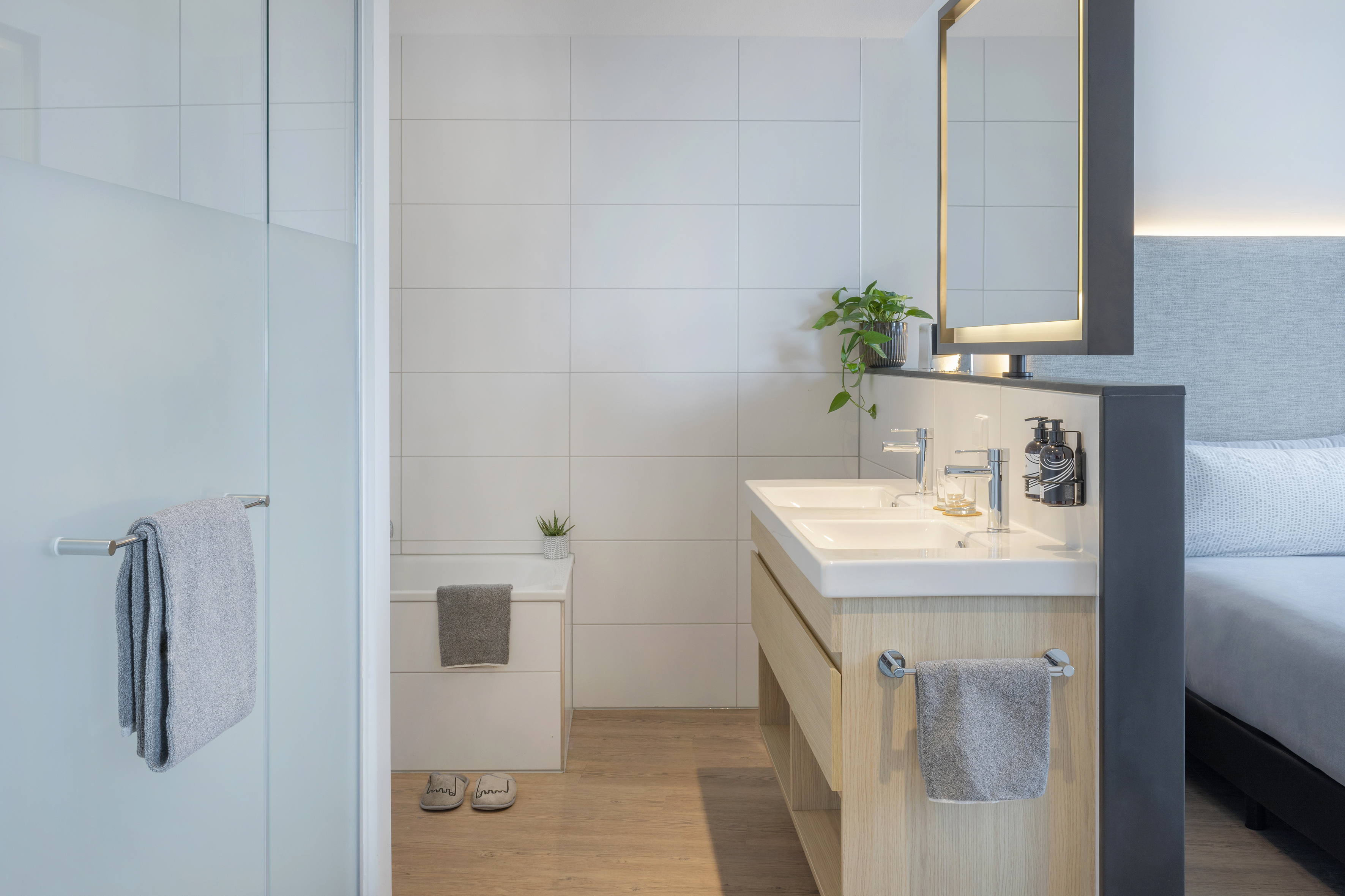 Modern hotel bathroom with double vanity, frosted shower, and clean white tiles.