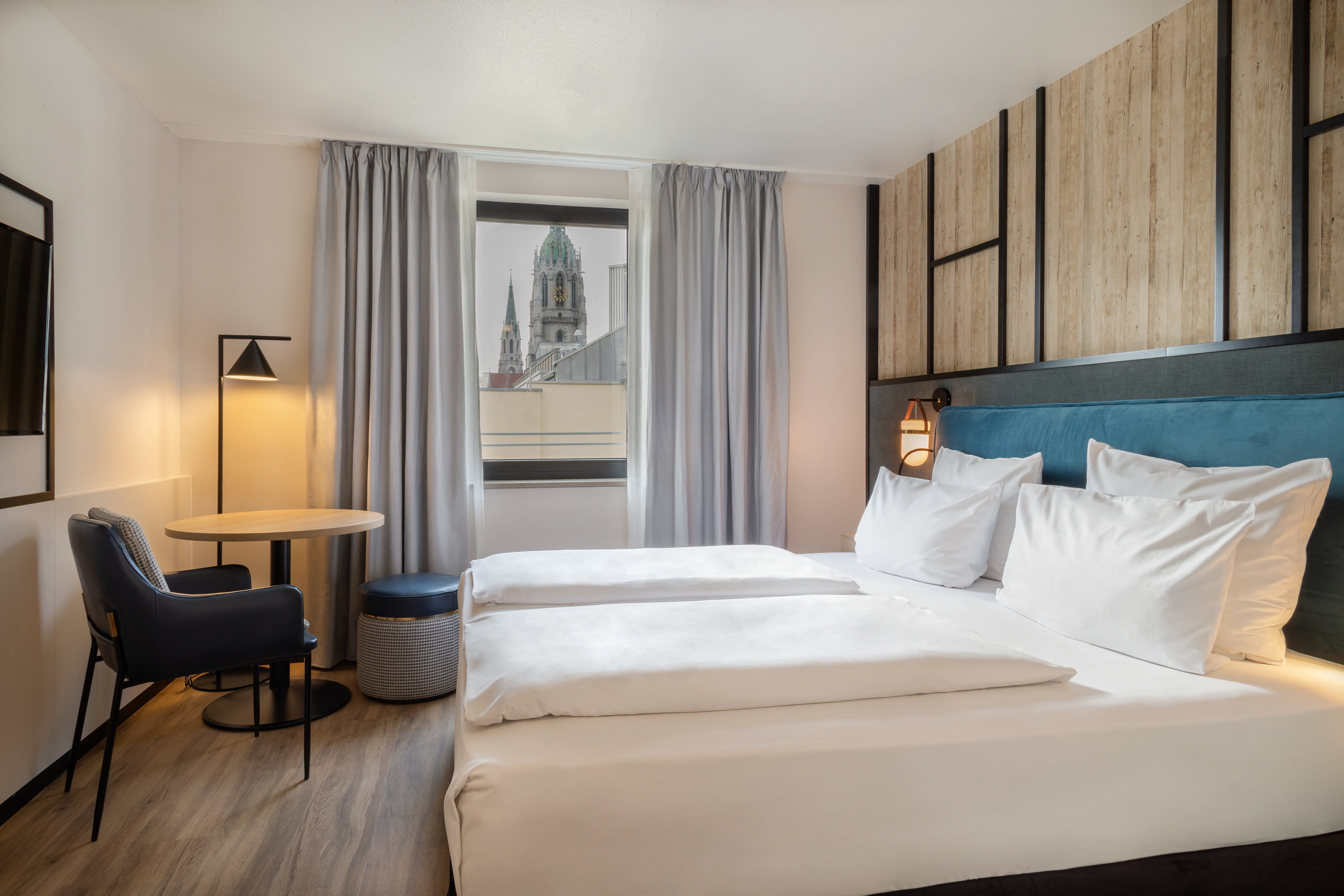 Modern hotel room with spacious bed, blue headboard, and city view.