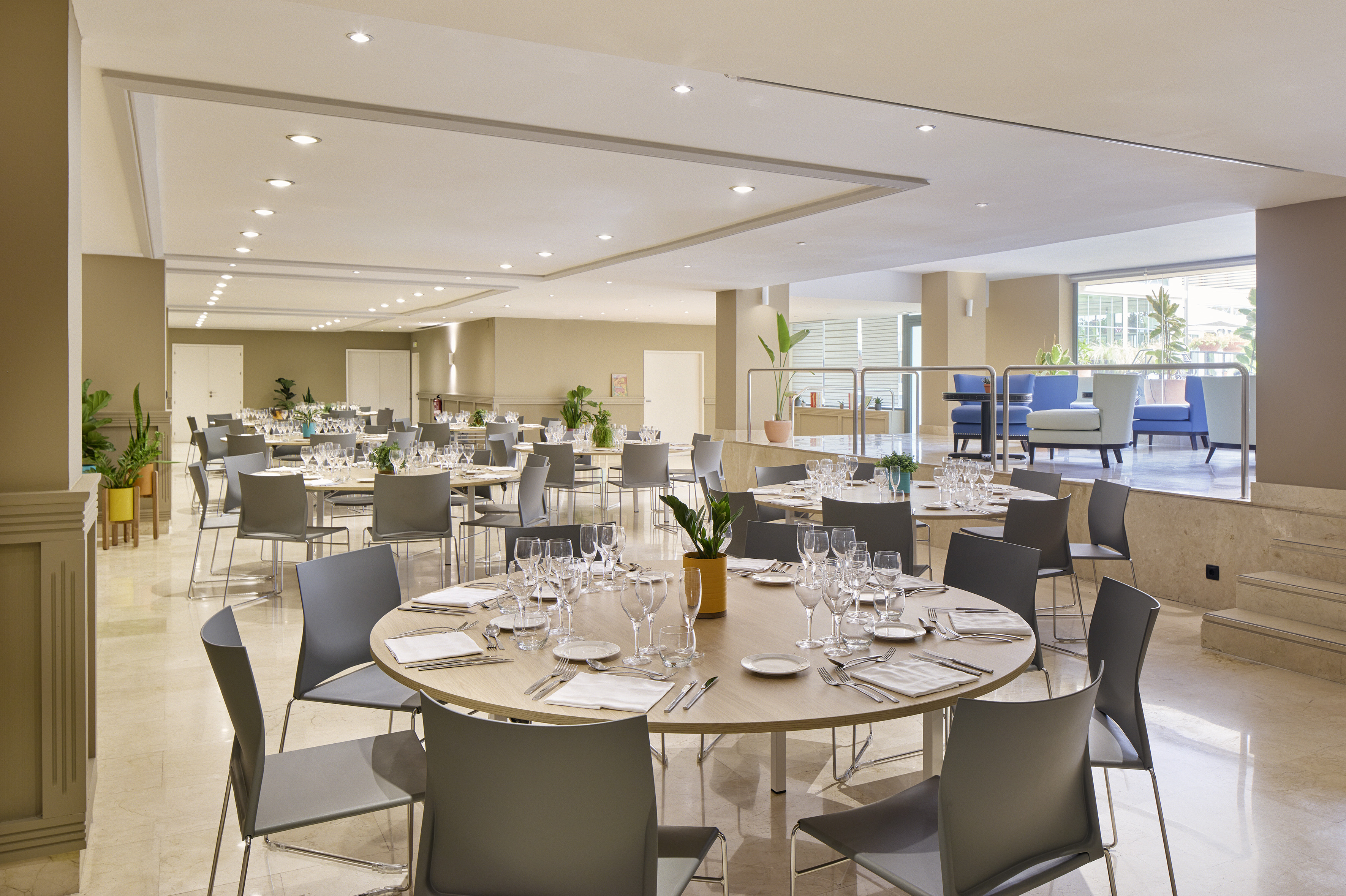Modern hotel banquet hall with set round dining tables and a lounge area.