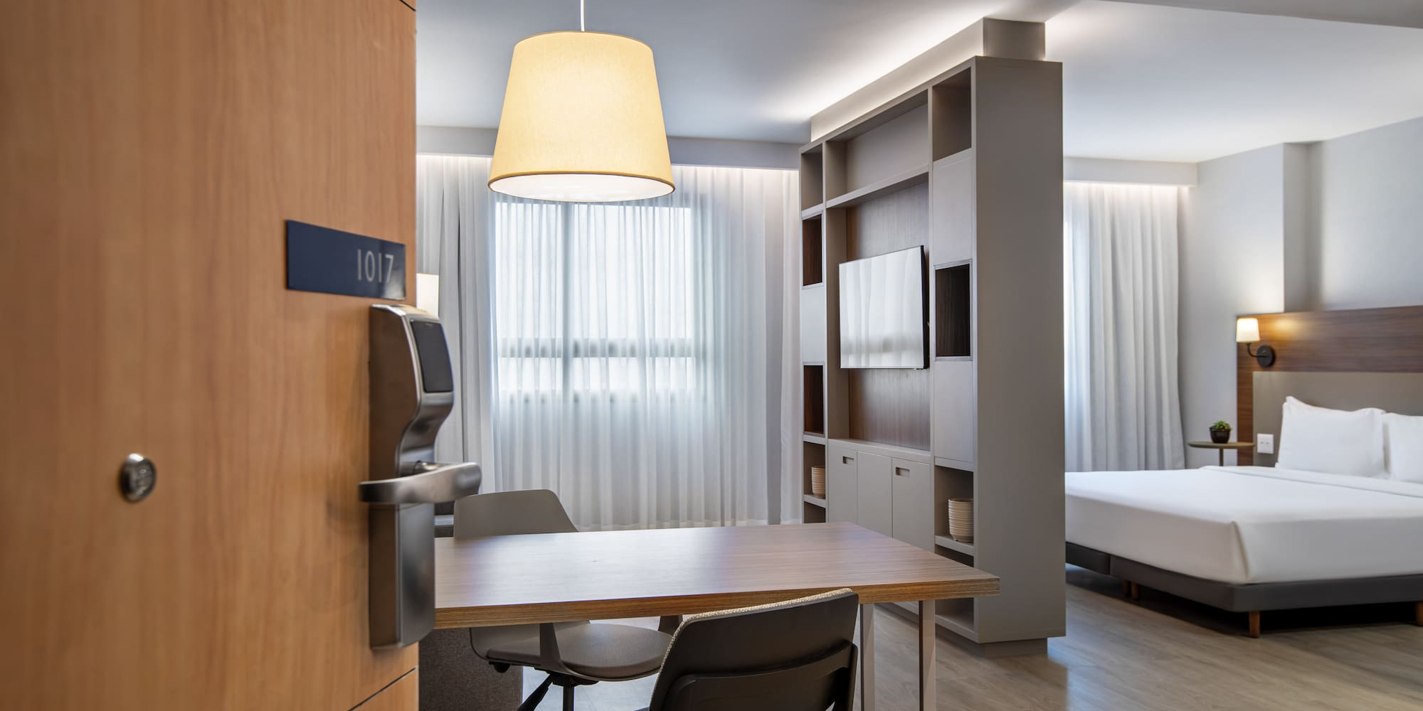 Modern hotel suite 1017 with bed, dining table, and TV unit.