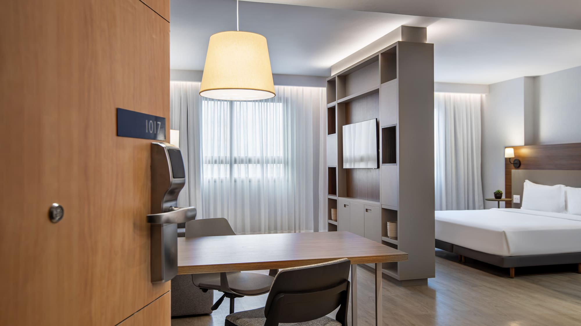 Modern hotel suite 1017 with bed, dining table, and TV unit.