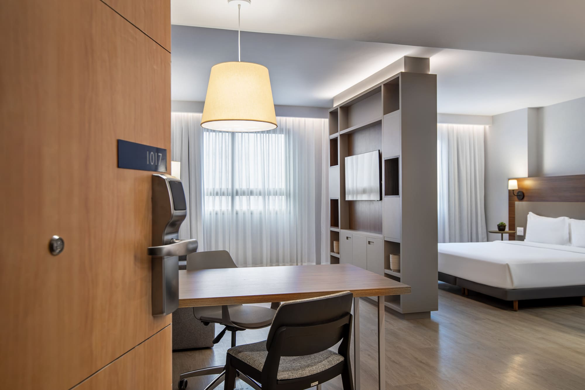Modern hotel suite 1017 with bed, dining table, and TV unit.